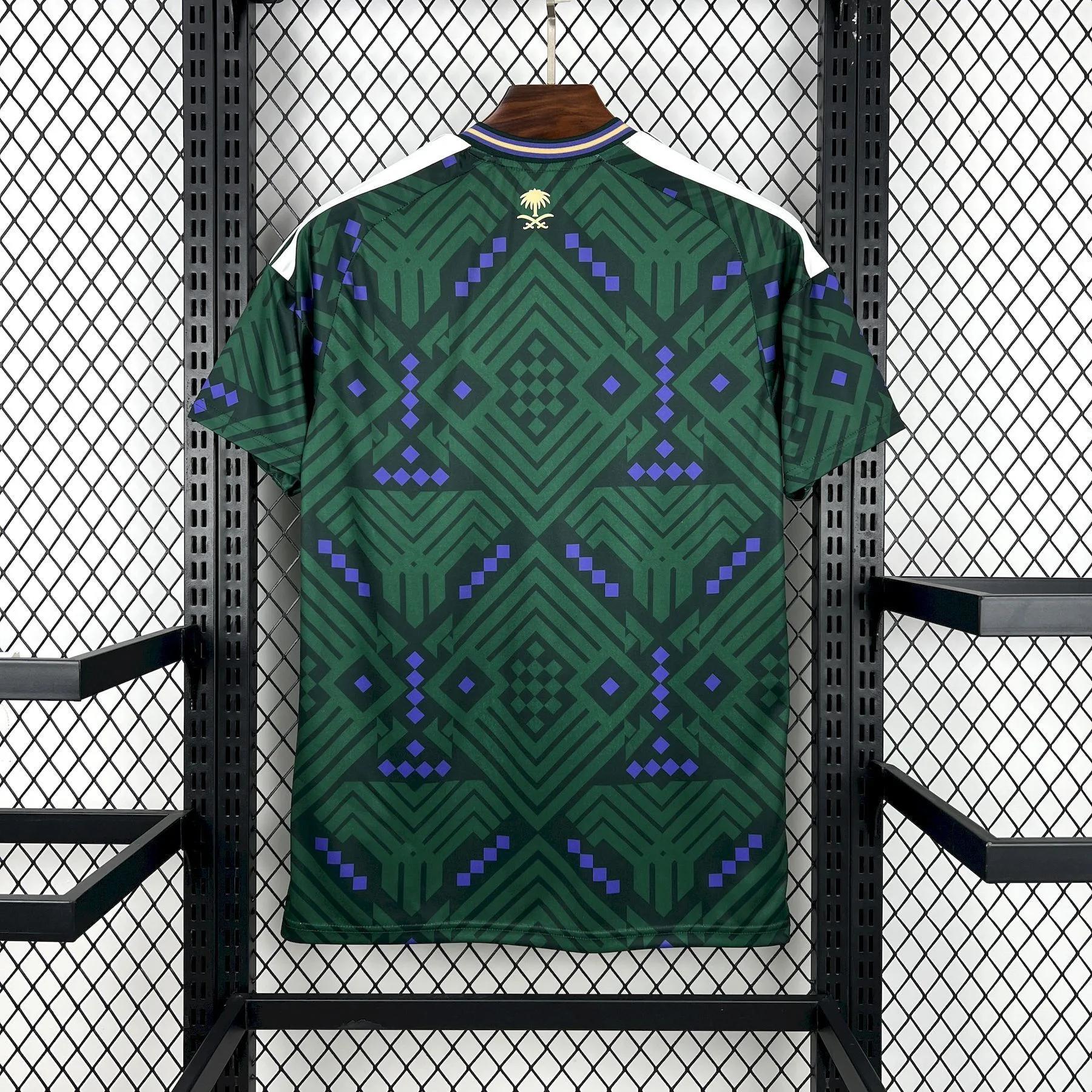 Vista trasera de la camiseta de Arabia Saudita para el Mundial 2026, con patrón geométrico verde y el emblema de la palmera y las espadas en dorado en la nuca.