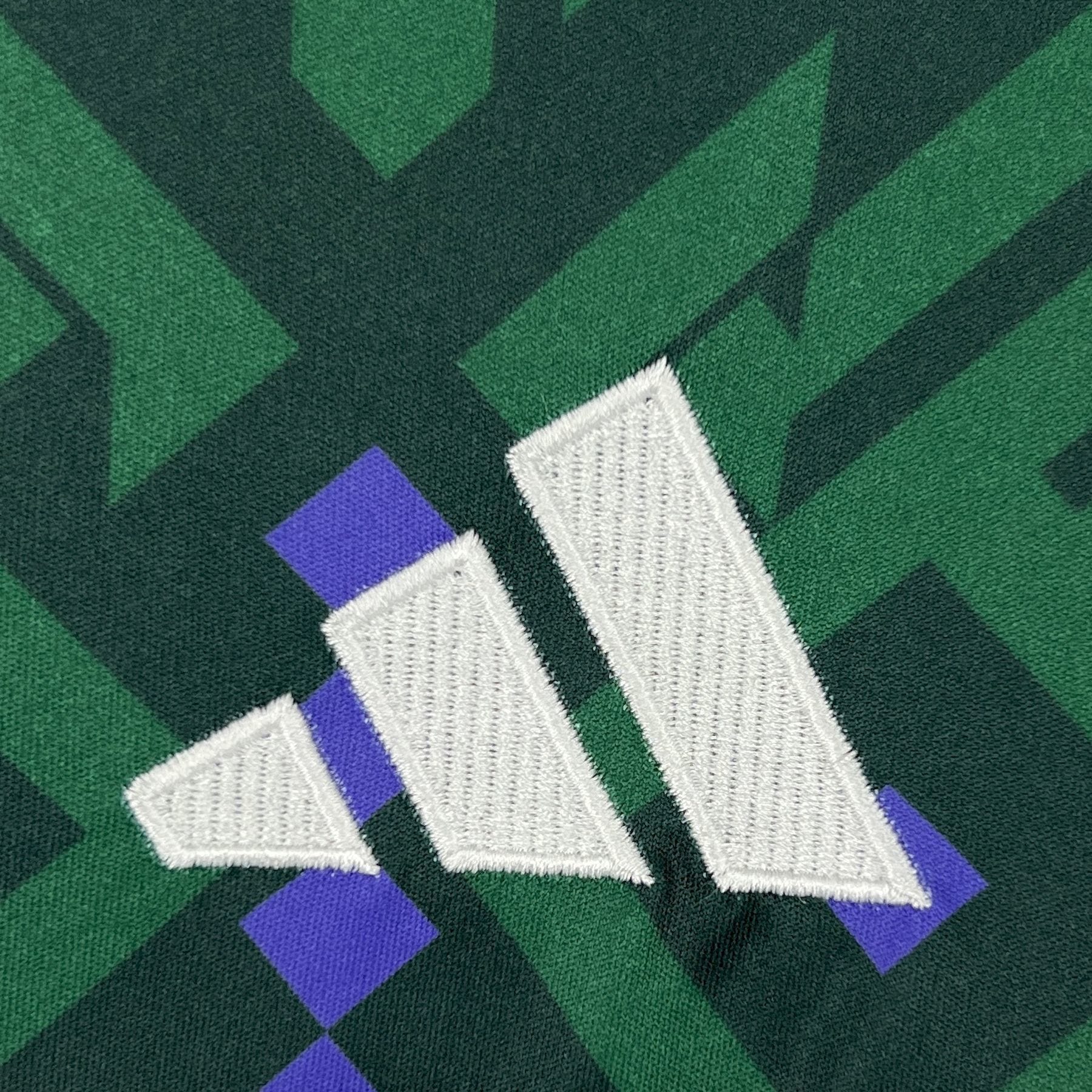 Camiseta de la selección de Arabia Saudita para el Mundial 2026, destacando el logotipo de la marca bordado en blanco sobre el patrón geométrico verde y violeta.