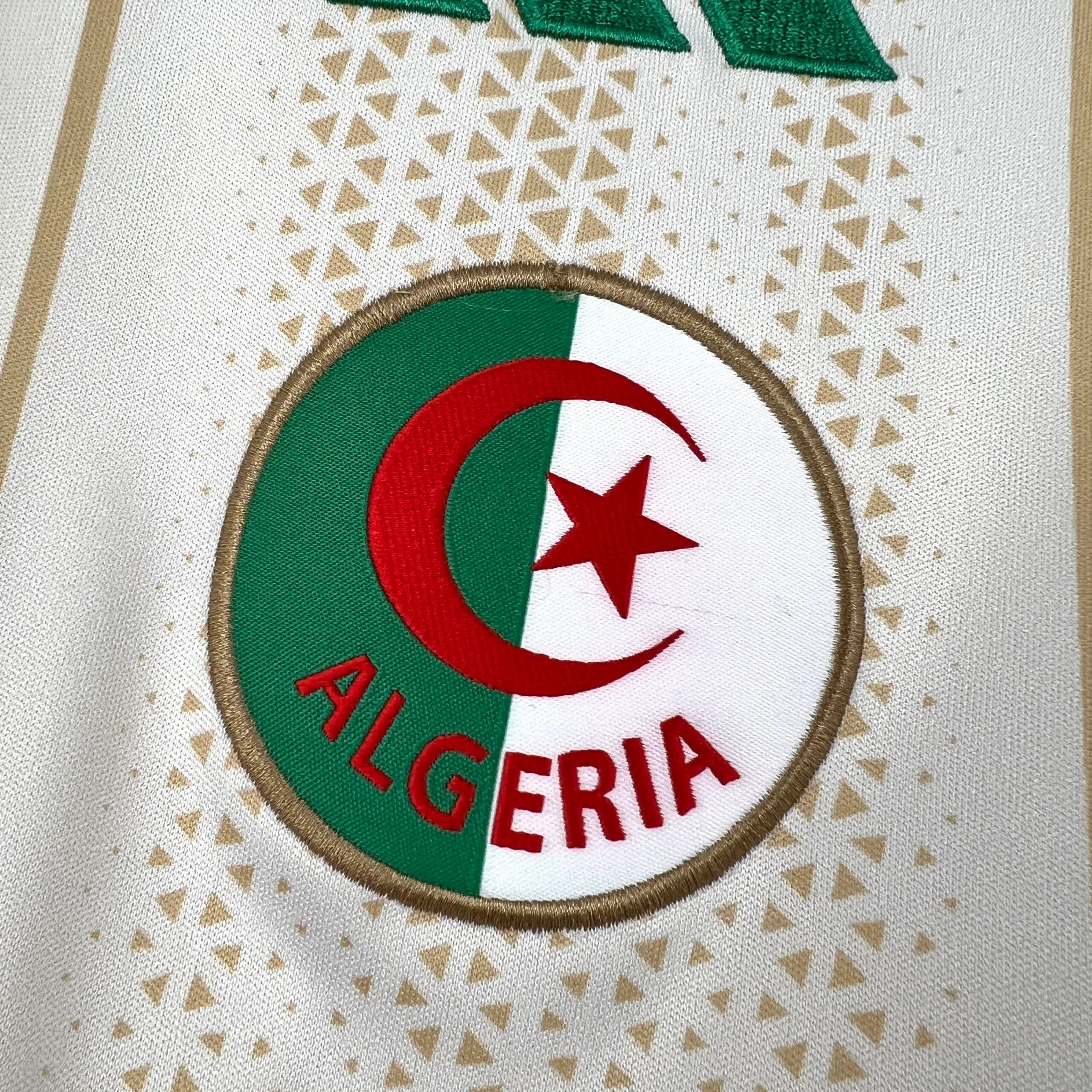 Primer plano del escudo de la selección de Argelia bordado con la luna y la estrella en verde y rojo.