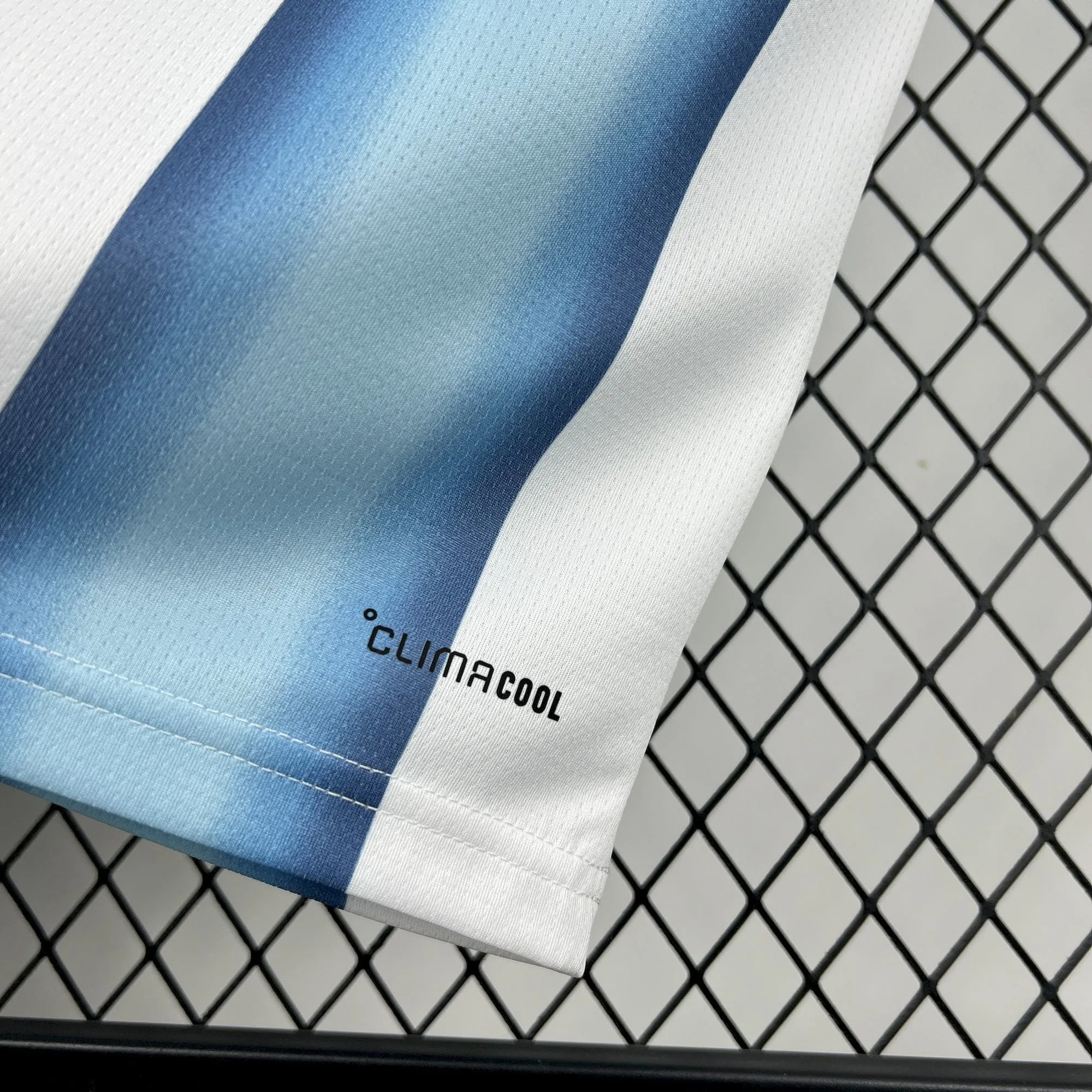 Detalle del logotipo Climacool impreso en negro sobre el dobladillo inferior de la camiseta de Argentina, junto a una franja celeste degradada.