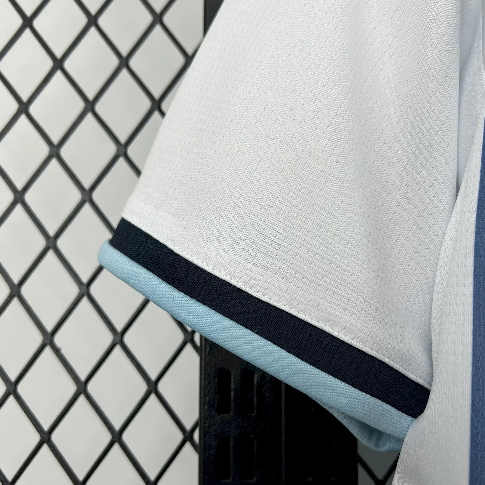 Primer plano del acabado de la manga blanca de la camiseta de Argentina, mostrando el ribete elástico con doble franja en color azul marino y celeste.