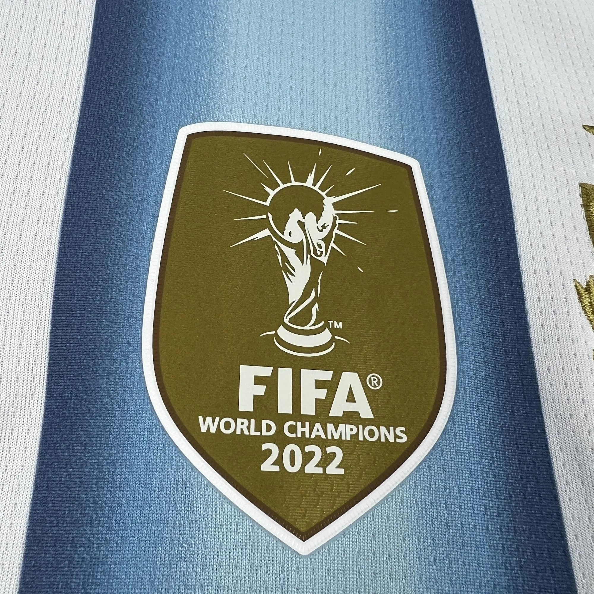 Primer plano del parche dorado de "FIFA World Champions 2022" termosellado en el centro del pecho de la camiseta argentina.