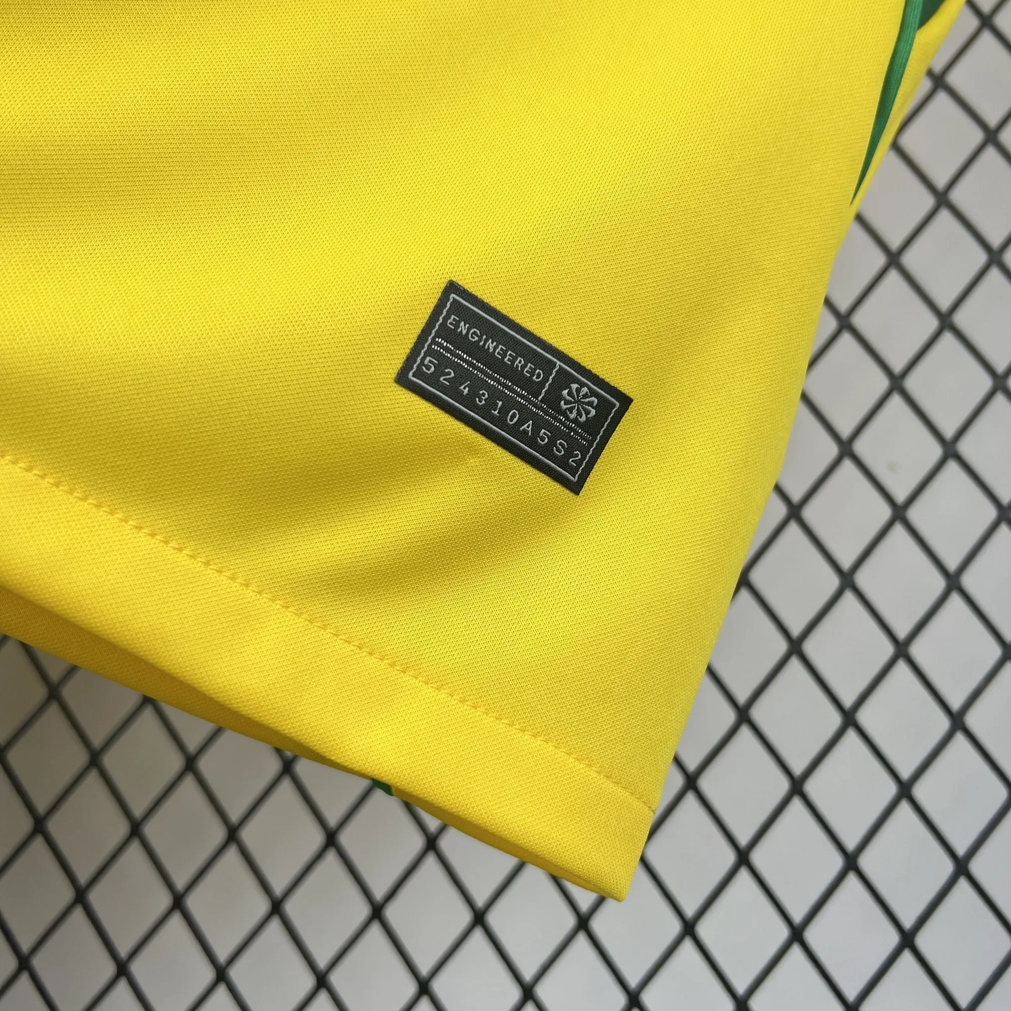 Detalle de un parche negro rectangular con la inscripción "ENGINEERED" y un código de serie único, cosido cerca de la base de la camiseta.