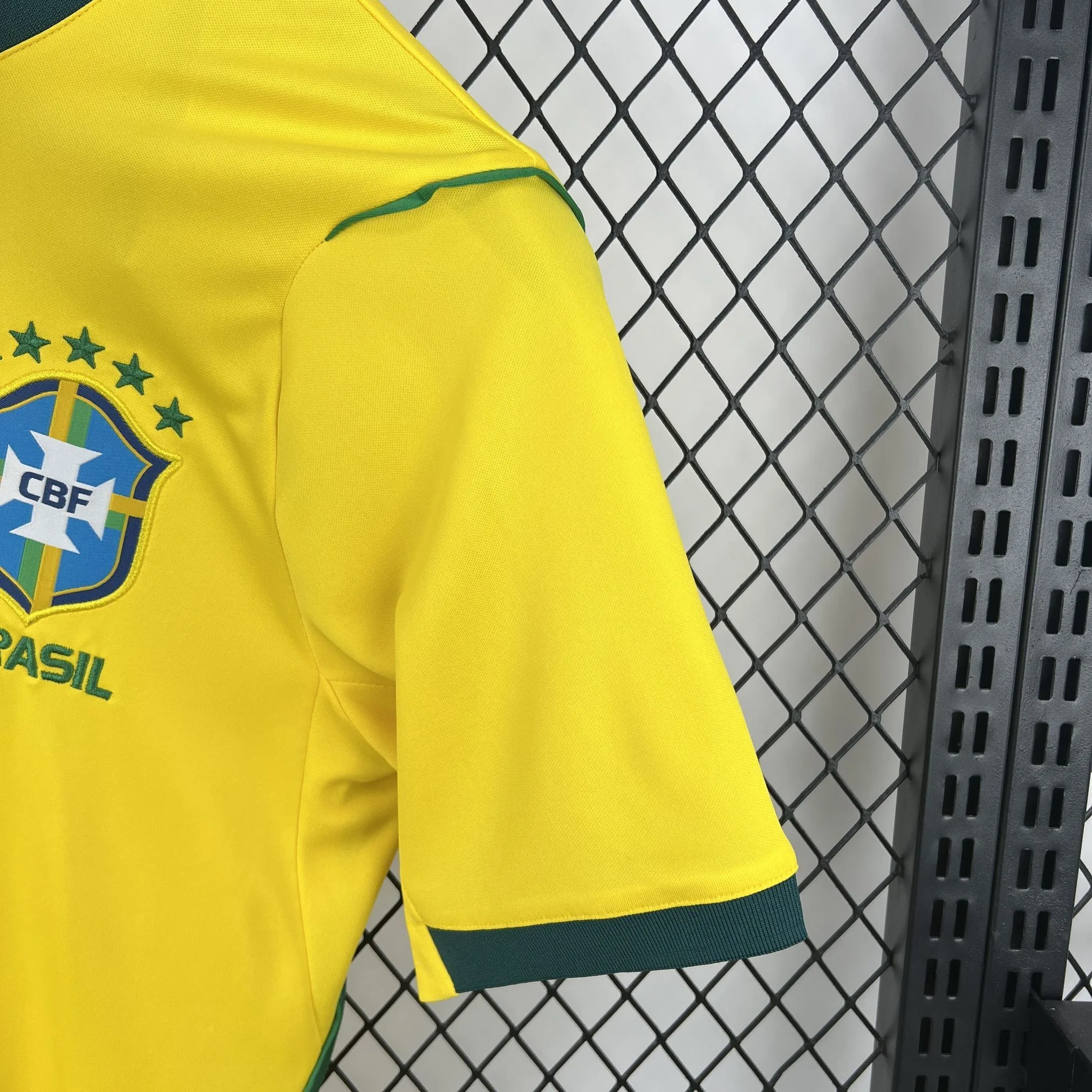 Vista lateral que muestra la unión de la manga amarilla con el panel frontal, destacando el escudo de la CBF y el ribete verde del cuello.