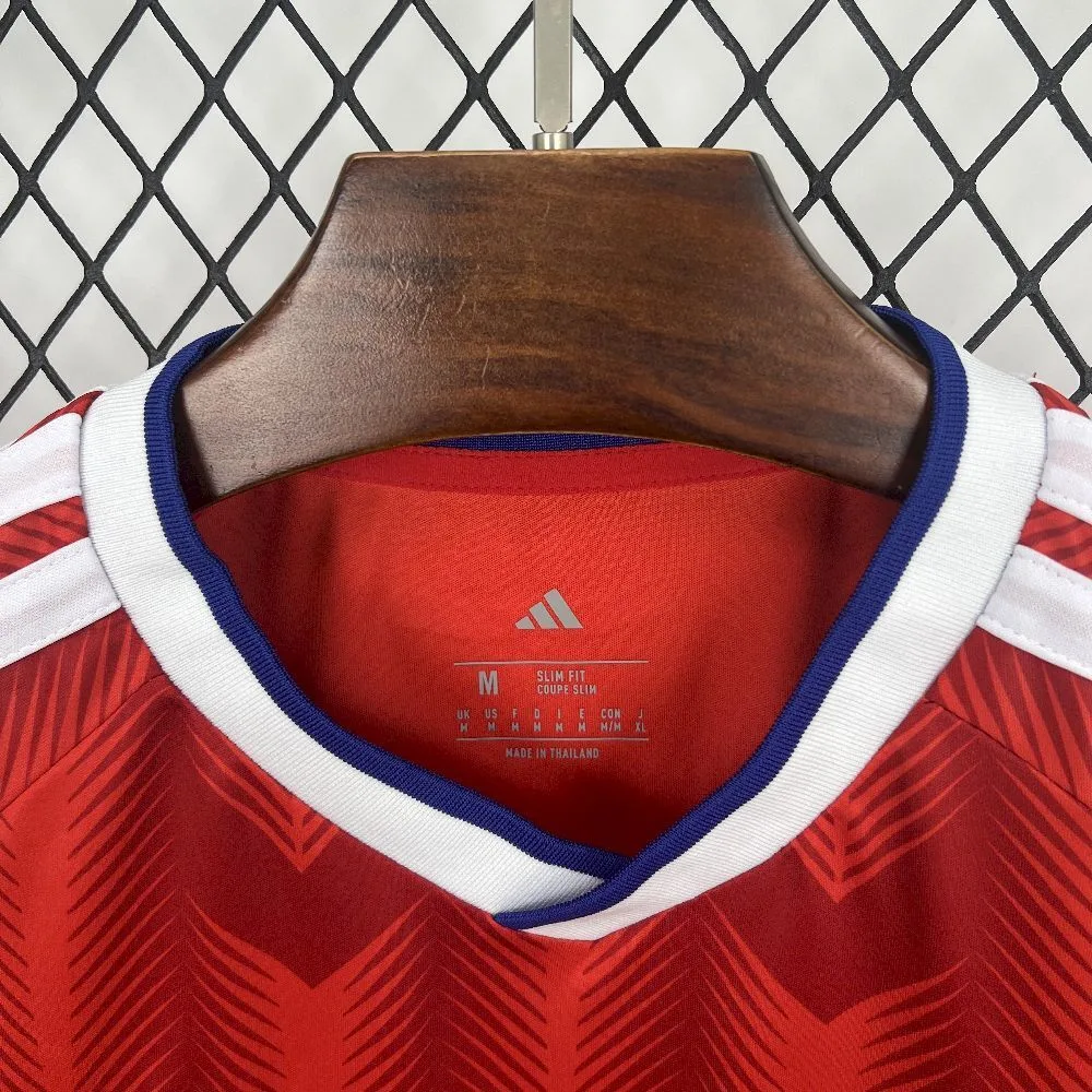 Detalle del interior del cuello en V de la camiseta de Chile, mostrando el ribete bicolor en blanco y azul, el gráfico de un cóndor en azul sobre el logotipo de la marca y etiquetas técnicas que indican talla M, corte "Slim Fit" y fabricación en Tailandia.