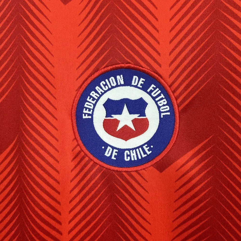 Primer plano del escudo de la Federación de Fútbol de Chile bordado sobre el patrón de flechas rojas.