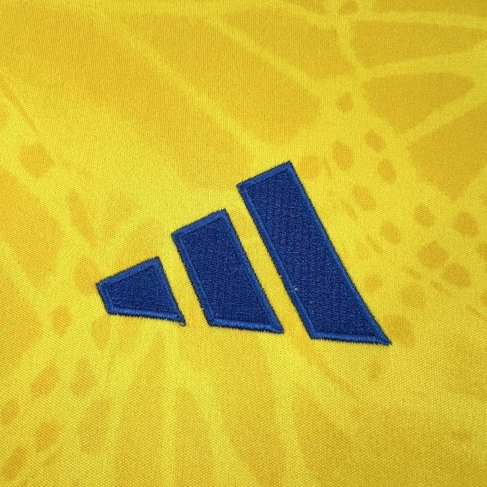 Detalle del logotipo de la marca bordado en azul sobre el patrón de mariposas amarillo.