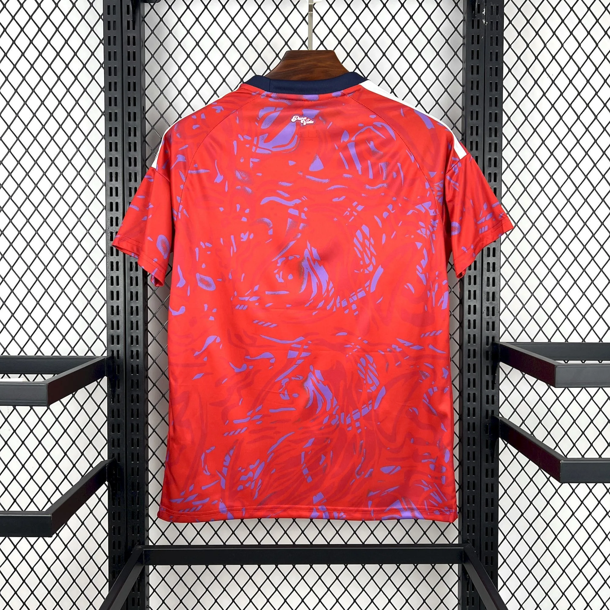 Parte posterior de la camiseta de Costa Rica que muestra la continuidad del patrón gráfico rojo y púrpura y un pequeño detalle decorativo en la nuca.