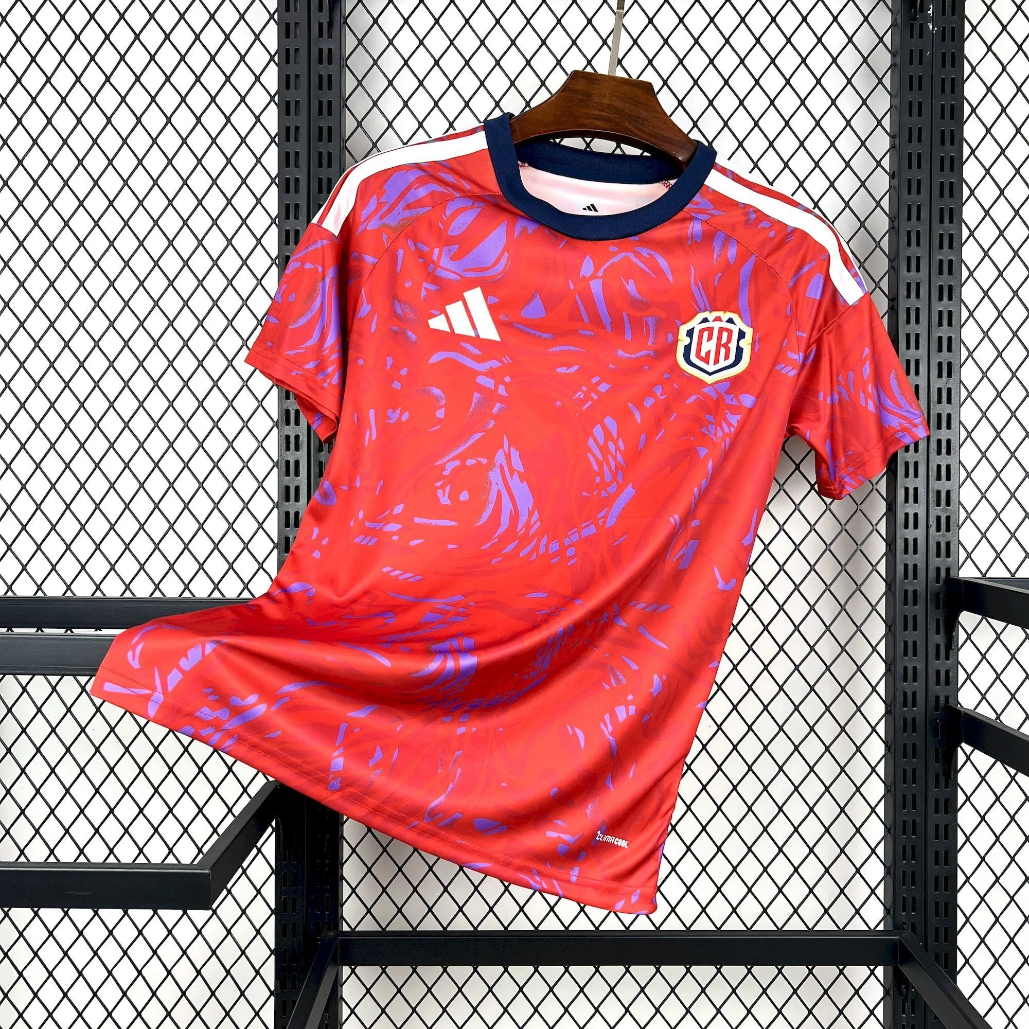Vista frontal de la camiseta de Costa Rica para el Mundial 2026, con un llamativo patrón gráfico abstracto en rojo y tonos púrpura, detalles blancos en los hombros y el nuevo escudo de la FCRF.