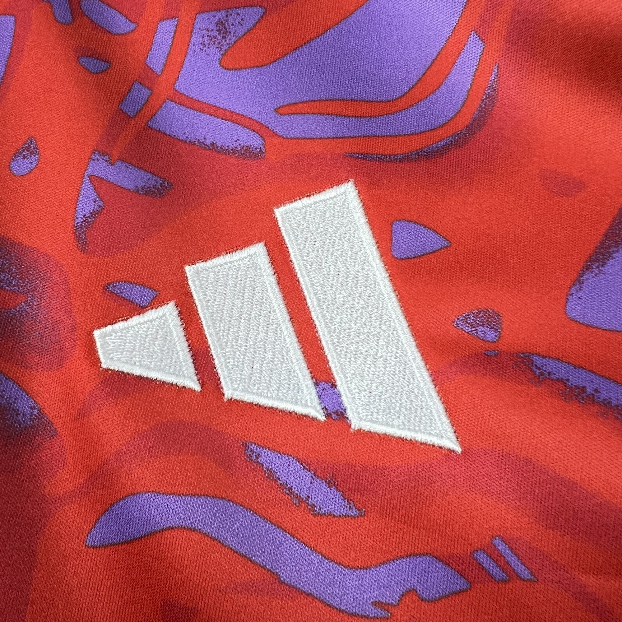 Detalle del logotipo de la marca bordado en hilo blanco sobre el tejido rojo con el patrón gráfico artístico de la equipación de Costa Rica.