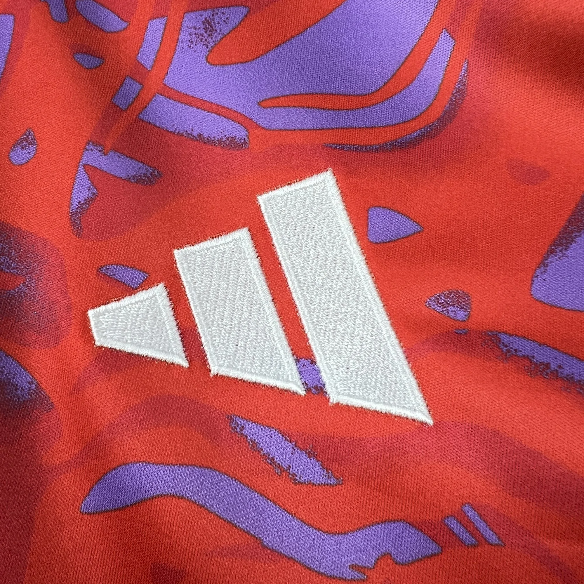 Detalle del logotipo de la marca bordado en hilo blanco sobre el tejido rojo con el patrón gráfico artístico de la equipación de Costa Rica.