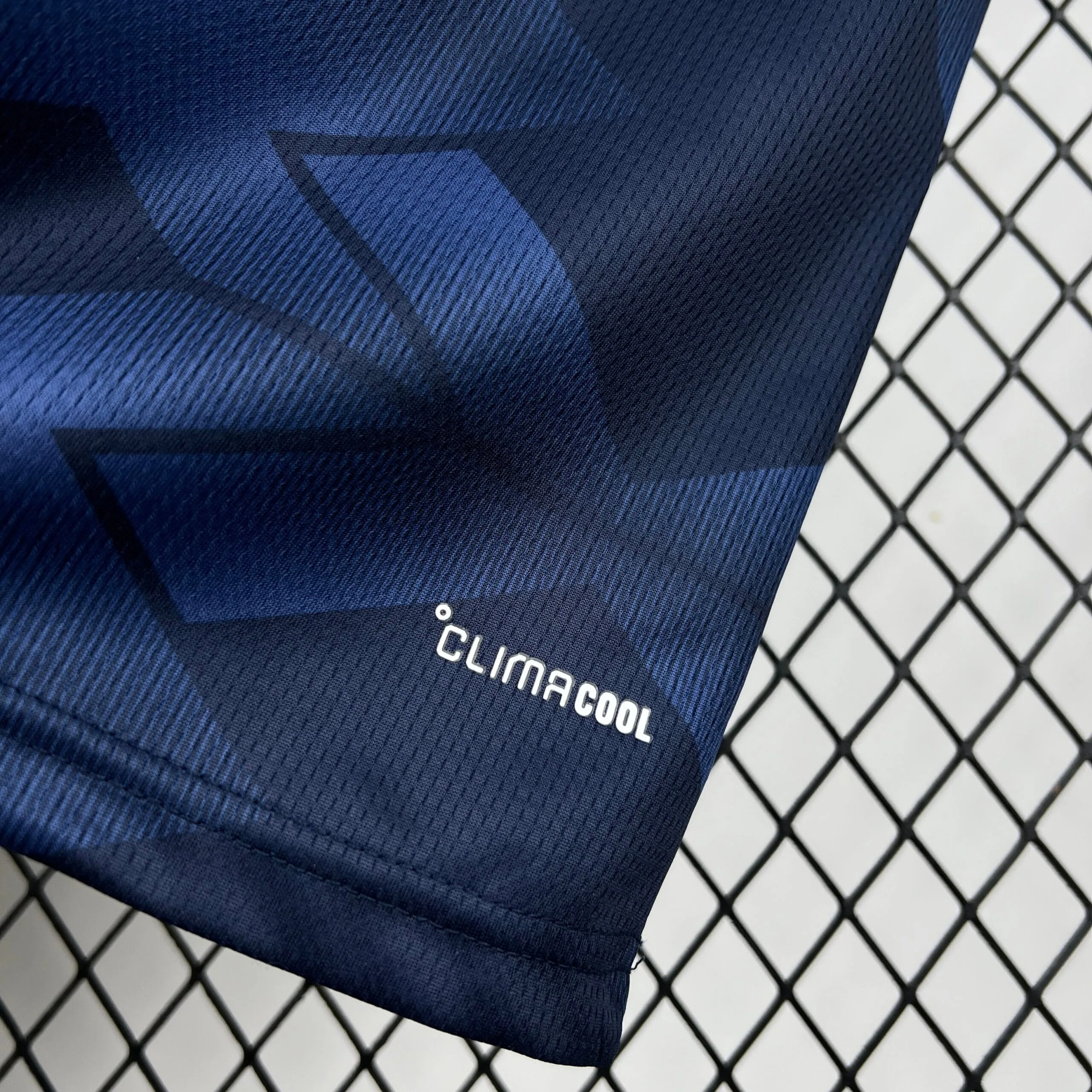 Detalle del sello de tecnología Climacool en color blanco, ubicado en el extremo inferior de la camiseta azul marino de Escocia.