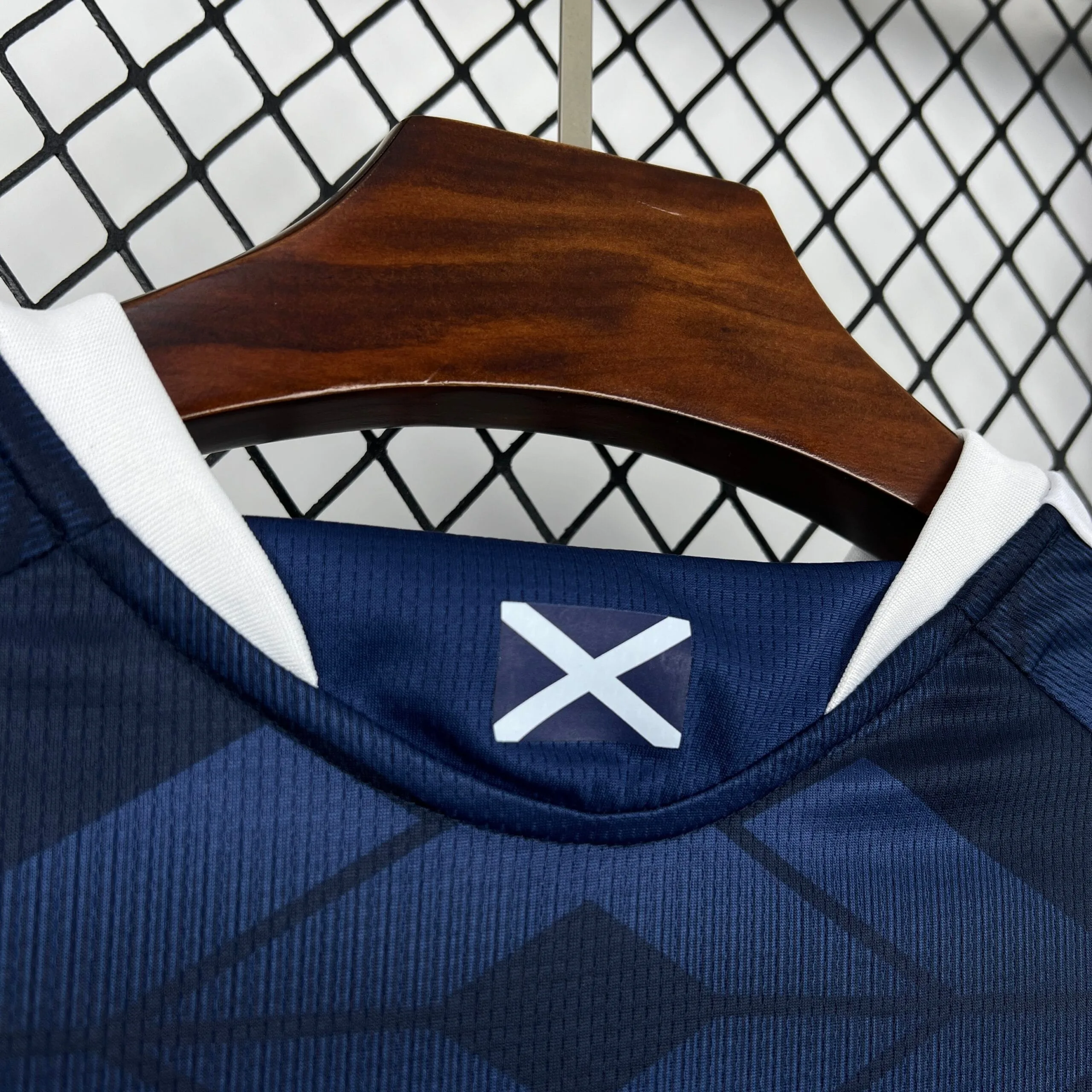 Detalle de la parte posterior del cuello de la camiseta de Escocia, con una pequeña bandera de San Andrés (aspa blanca sobre fondo azul) integrada en el diseño.