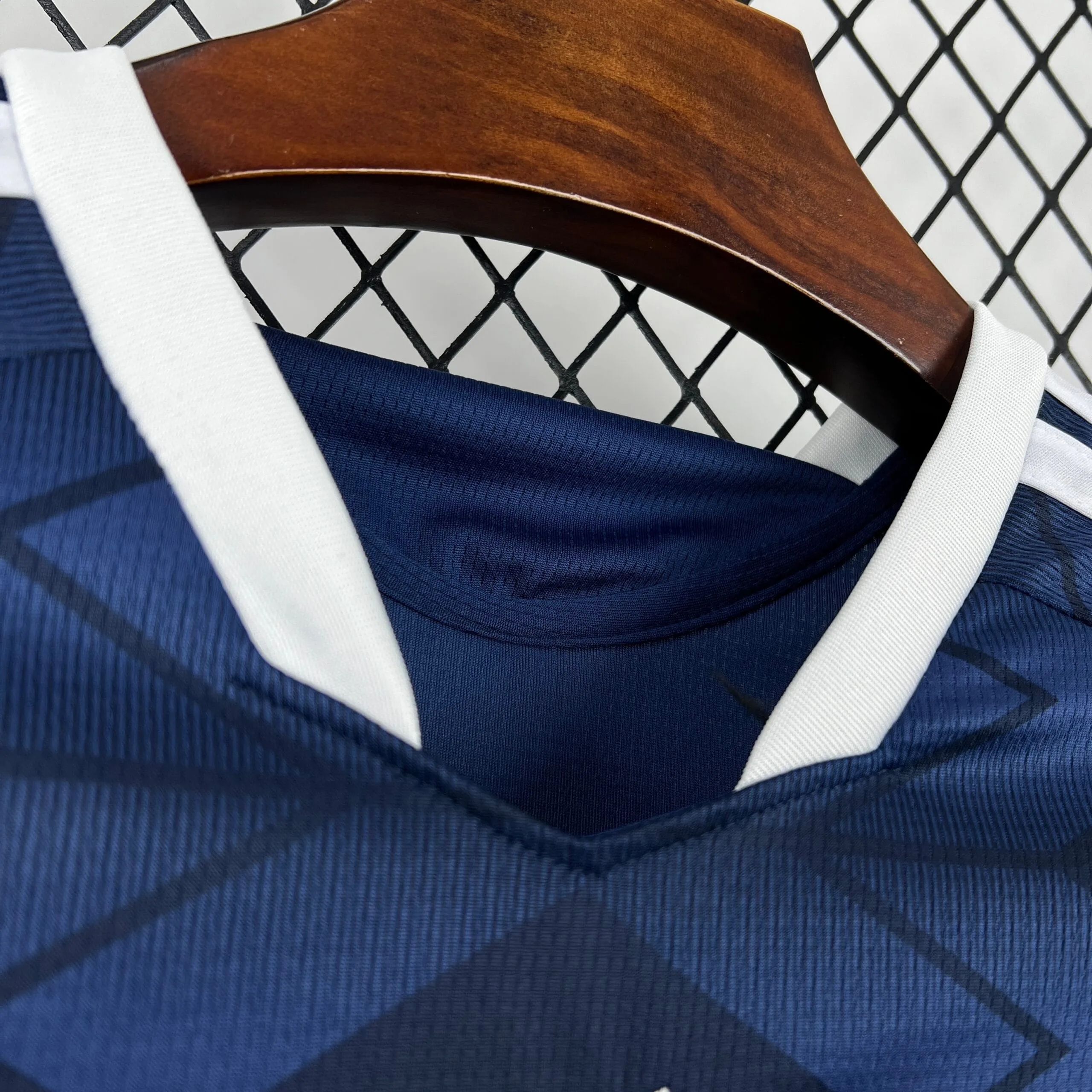 Primer plano del cuello cruzado en color blanco de la camiseta de Escocia, resaltando el tejido azul marino con patrón de rombos.