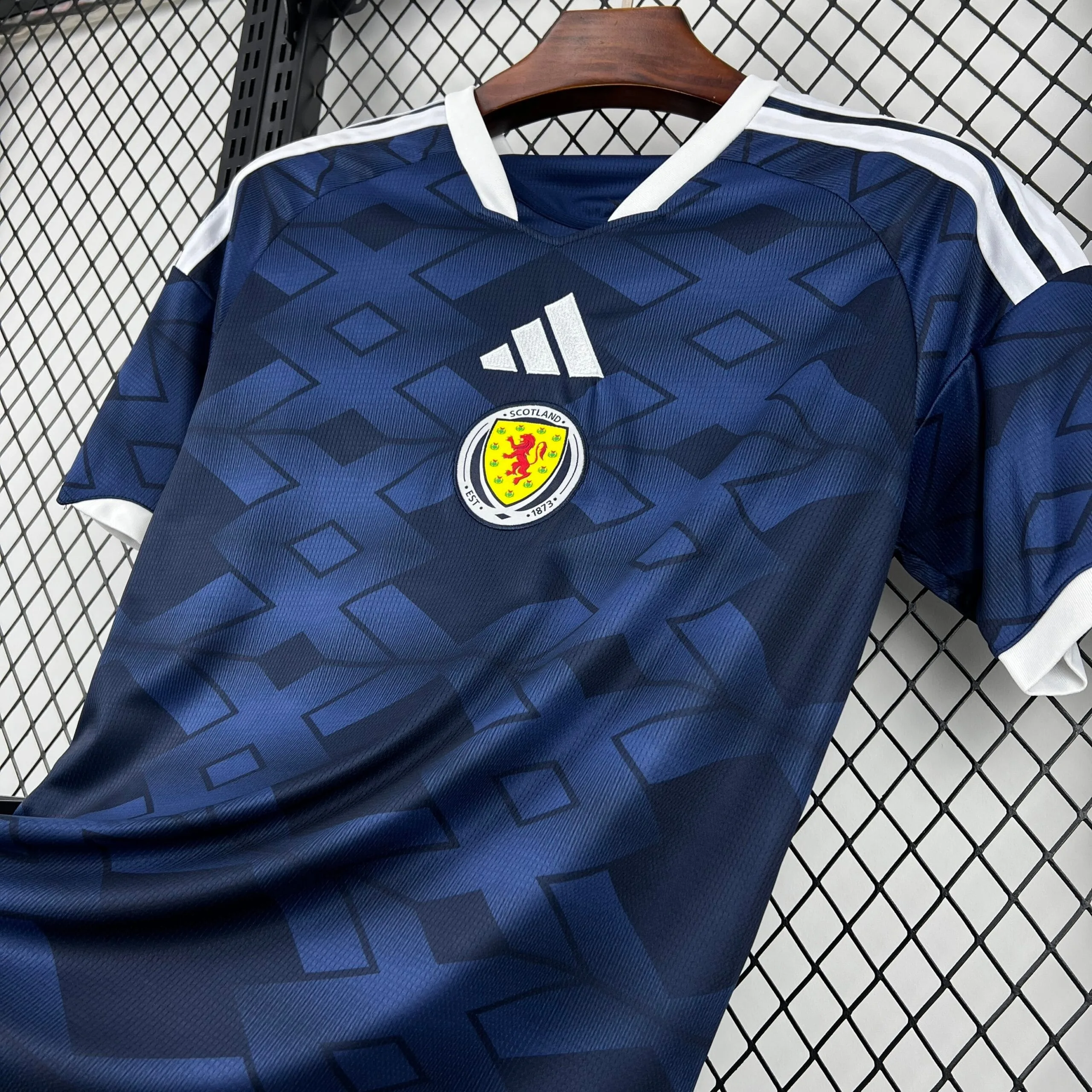 Camiseta oficial de la selección de Escocia en color azul marino con un patrón geométrico de rombos tonales, destacando el escudo circular de la federación en el centro y el logotipo de la marca en blanco.