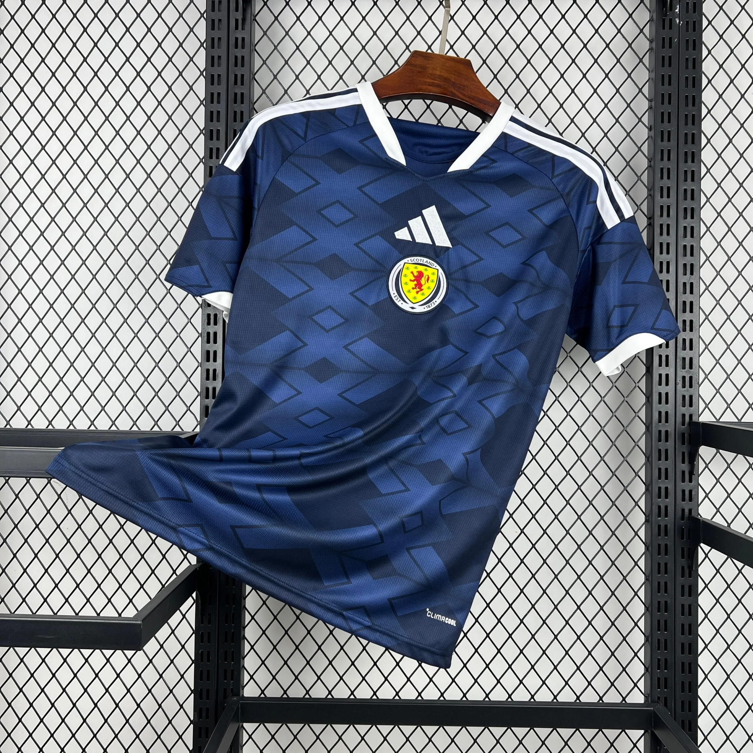 Imagen de la equipación completa de Escocia colgada en un soporte, resaltando el contraste entre el azul marino del cuerpo y los detalles blancos en cuello y hombros.