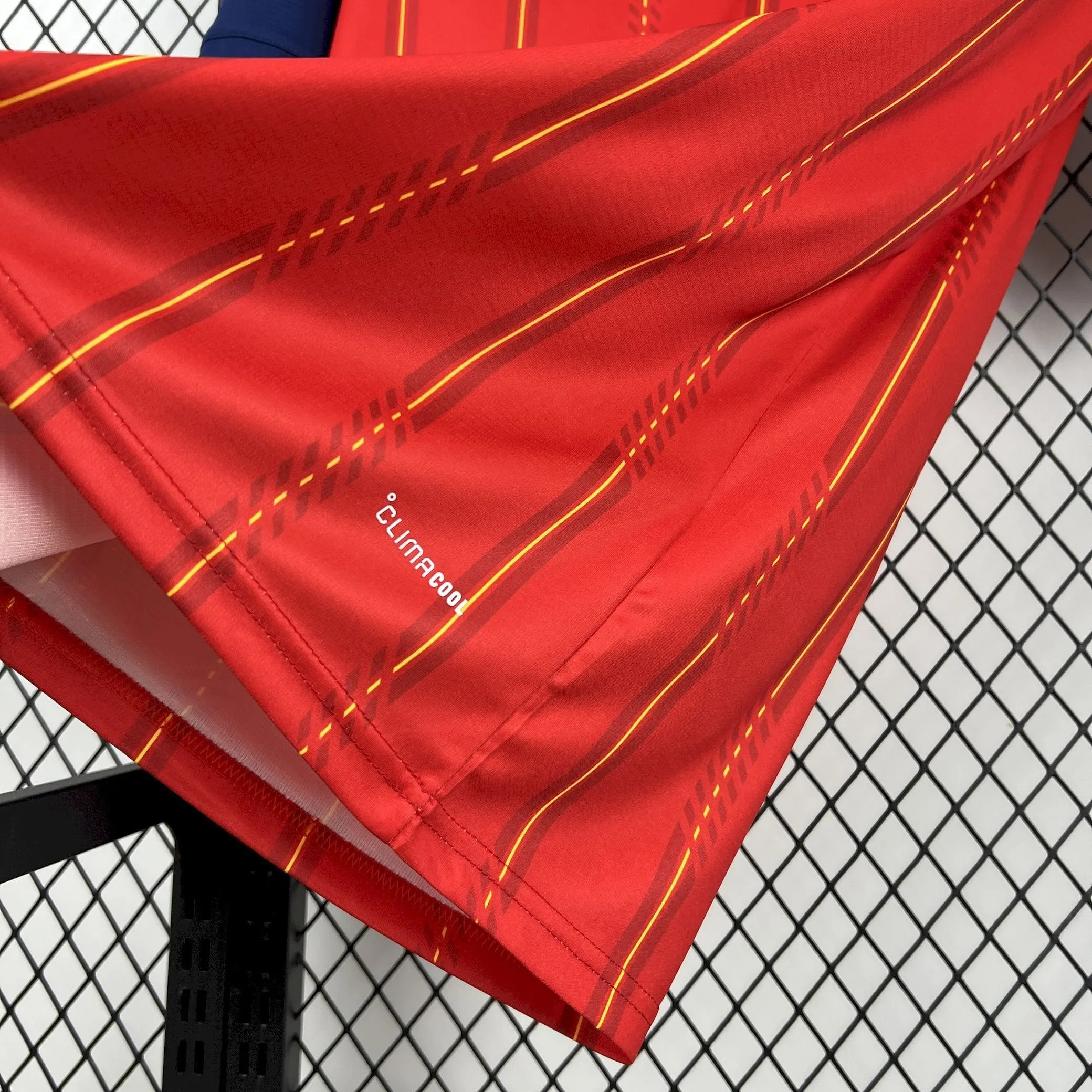Vista del dobladillo inferior de la camiseta de España mostrando el logotipo de la tecnología "Climacool" sobre el tejido rojo con patrón de líneas amarillas.