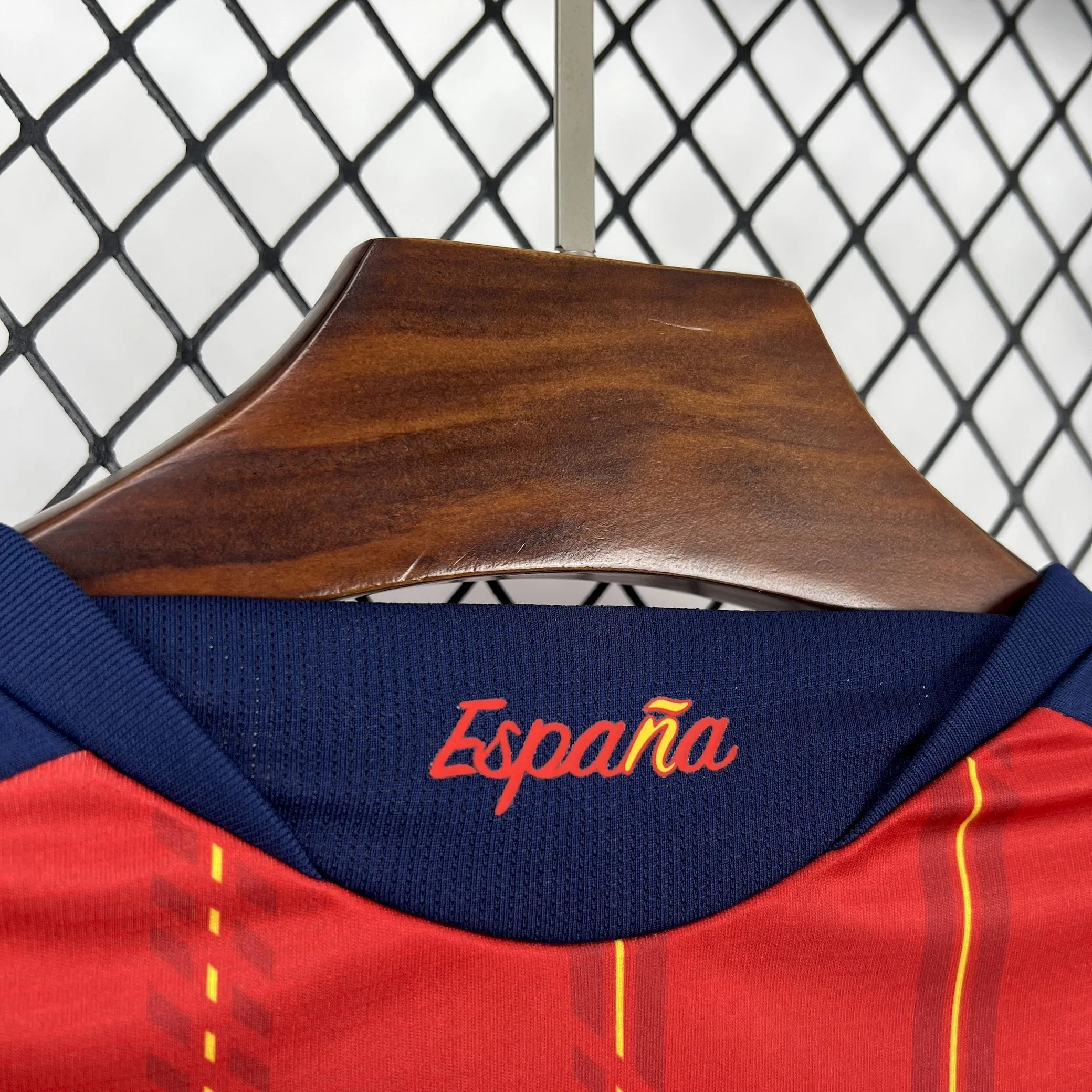 Primer plano del nombre "España" bordado en color amarillo y rojo en la zona posterior del cuello de la camiseta.