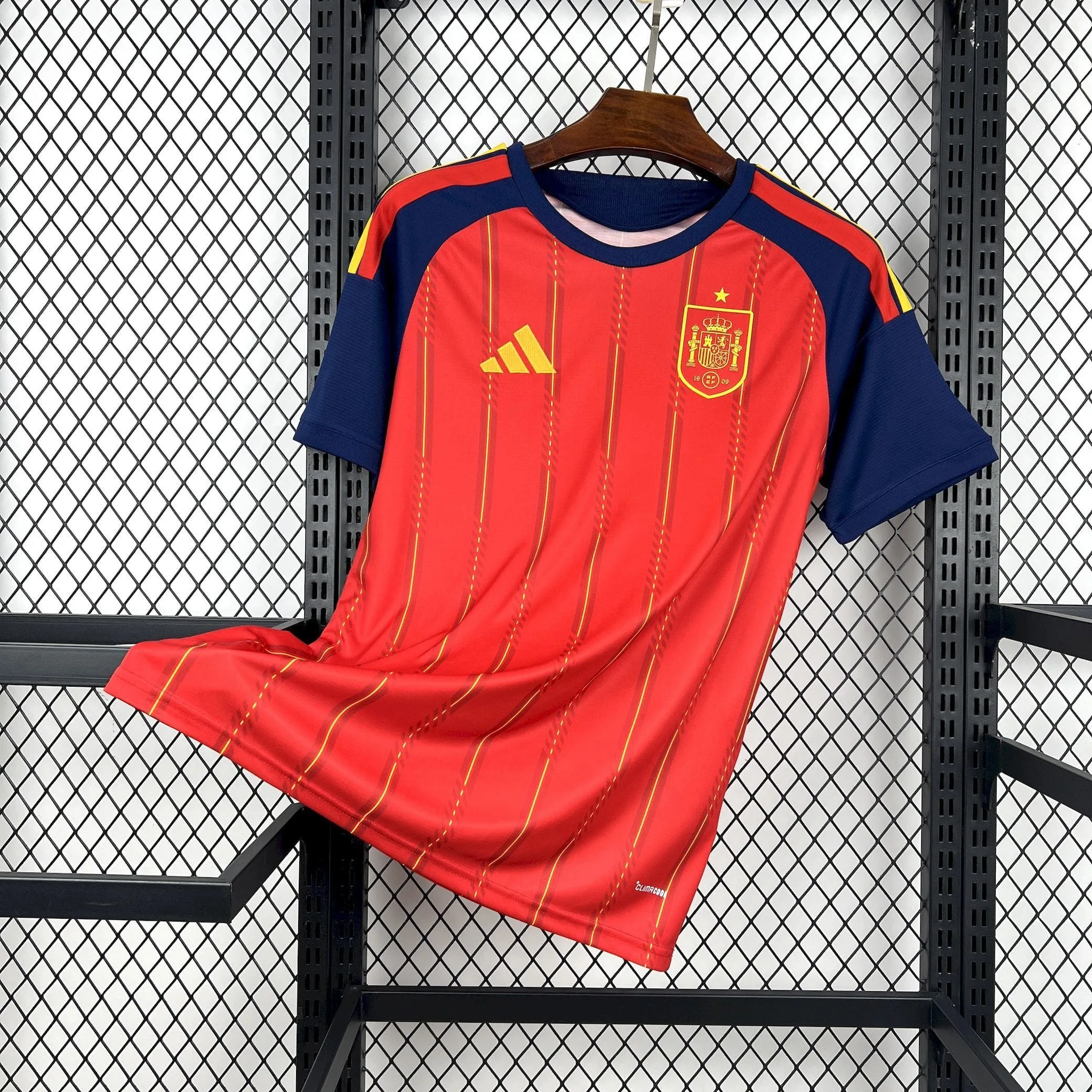 Vista frontal completa de la camiseta oficial de la selección española para el Mundial 2026, destacando el diseño de franjas verticales, el escudo en el pecho y las mangas azul marino.