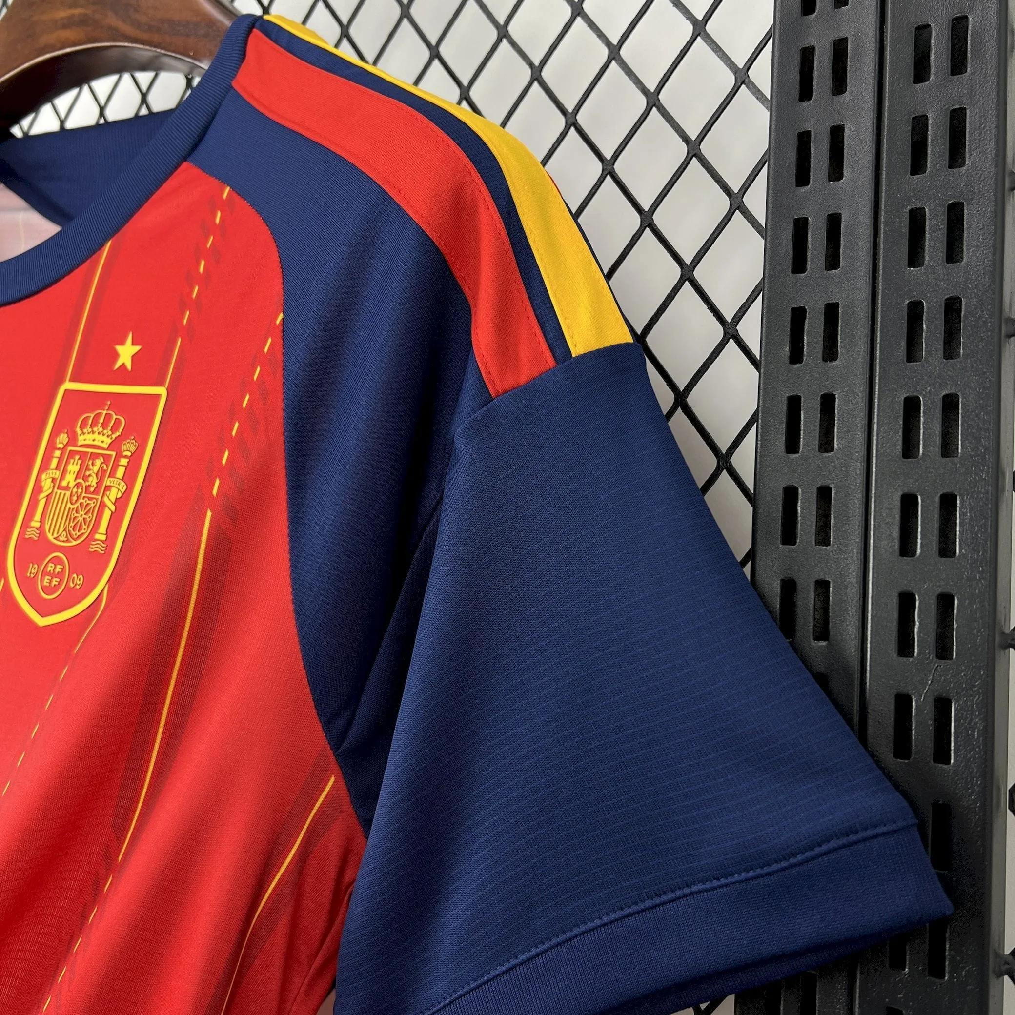 Detalle en primer plano del escudo de la selección española de fútbol con relieve de goma y estrella dorada sobre la camiseta roja del Mundial 2026.