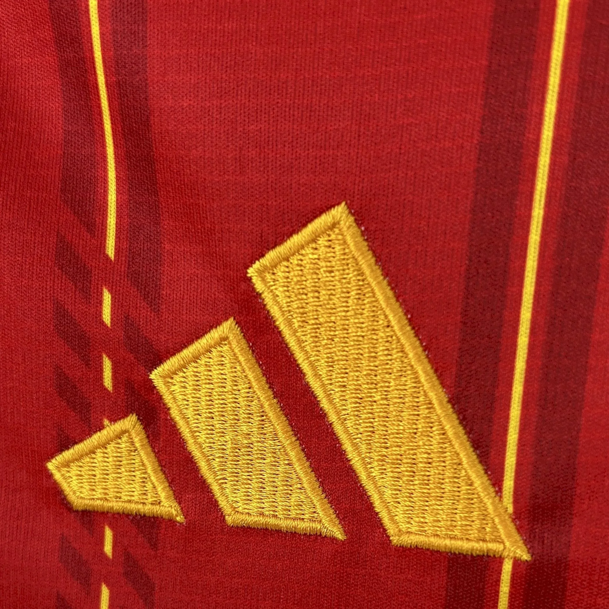 Primer plano del logotipo de la marca bordado en hilo amarillo de alta densidad sobre el tejido rojo de la camiseta.