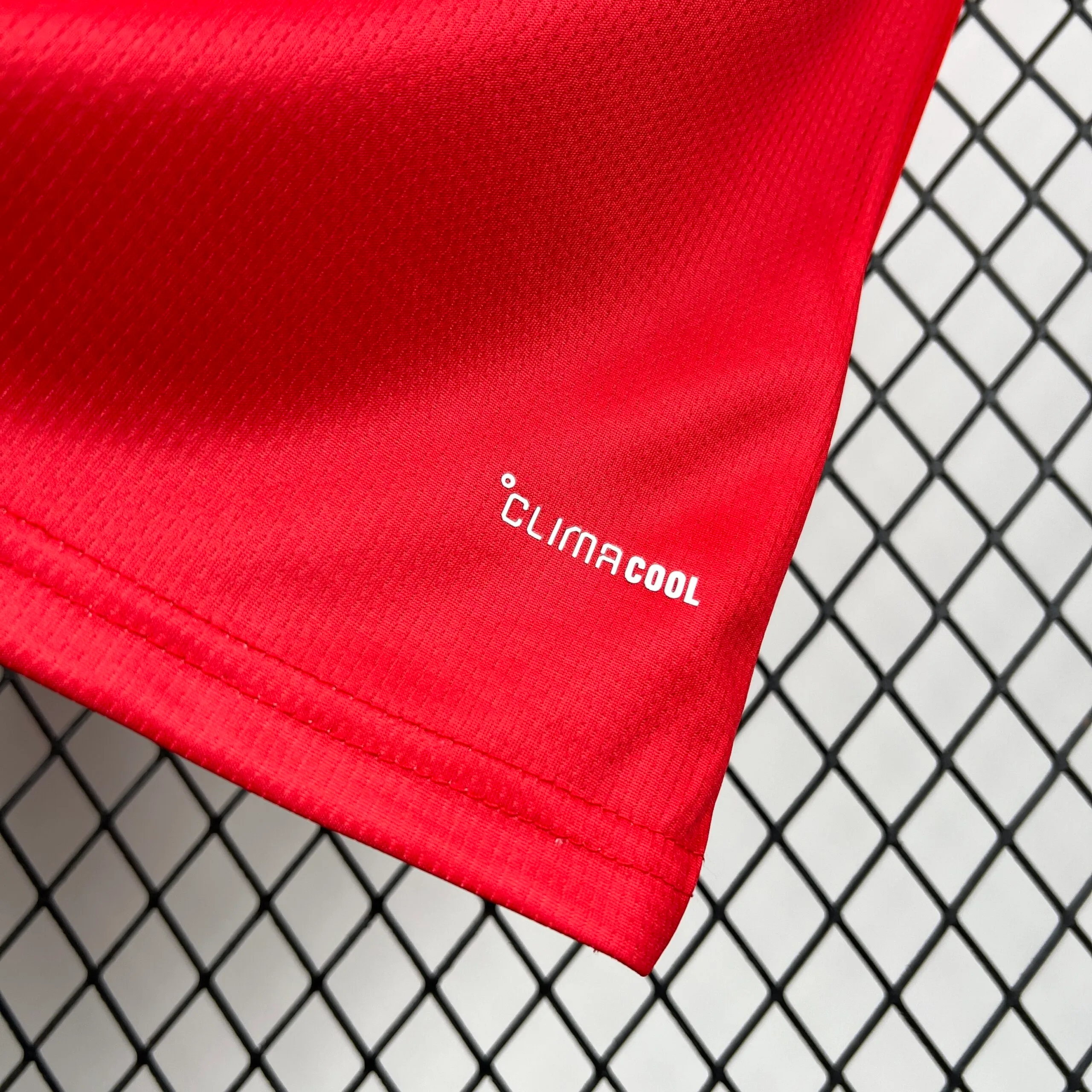 Primer plano del borde inferior de la camiseta roja, donde se aprecia el sello de la tecnología "CLIMACOOL" estampado en letras blancas sobre el tejido técnico microperforado.