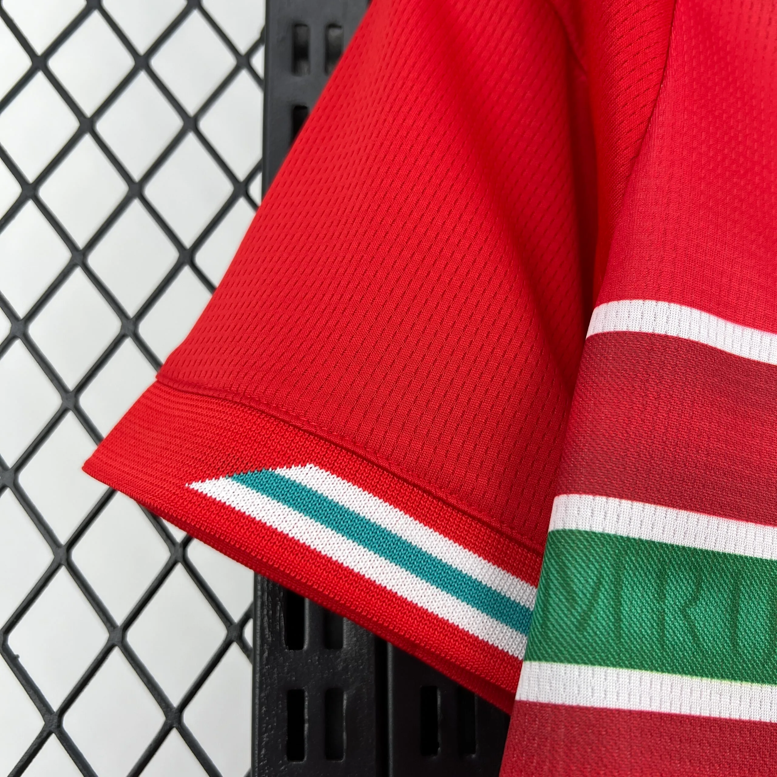 Detalle del puño de la manga de la camiseta de Gales, destacando el acabado en color rojo con un fino ribete de rayas blancas y verdes en el extremo.