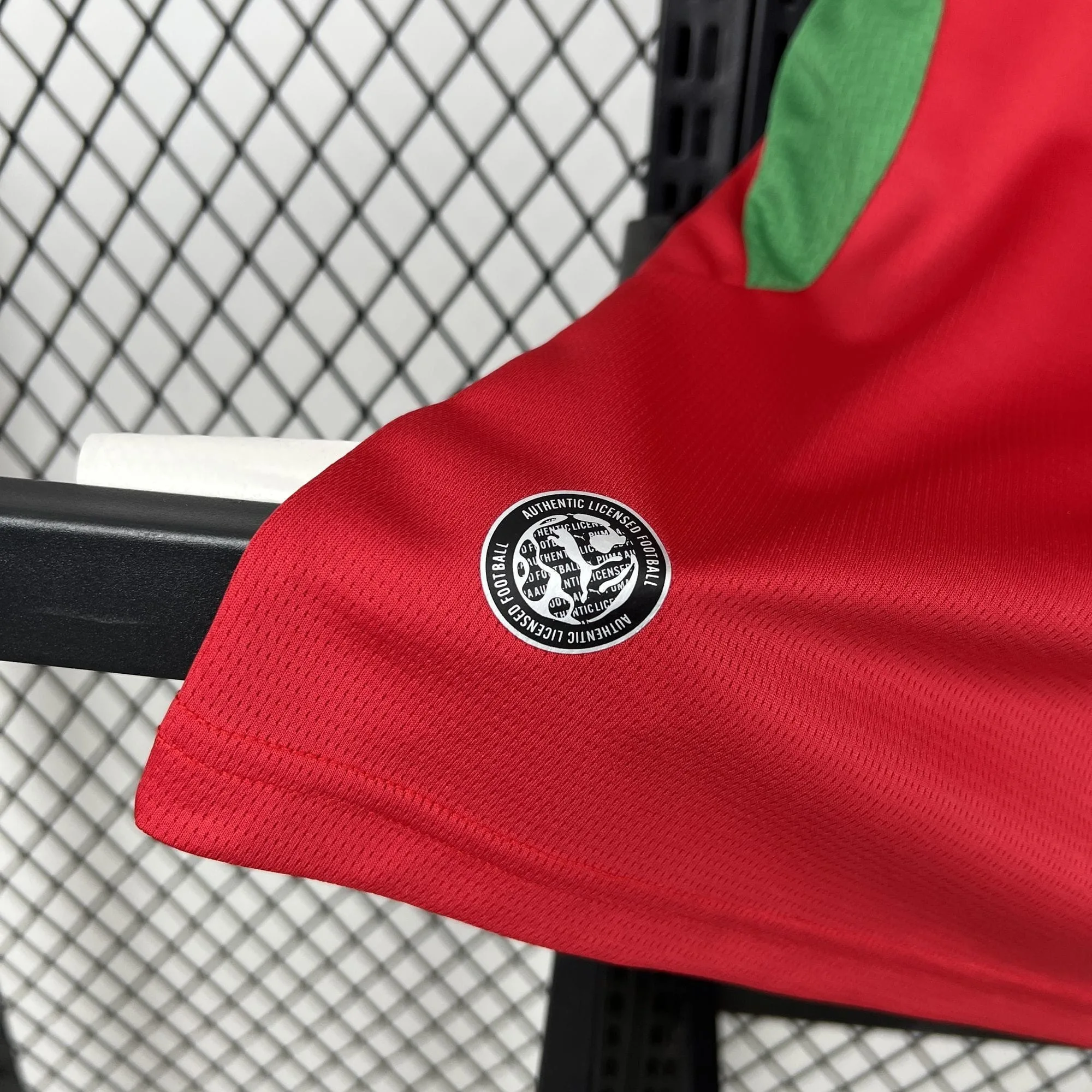 Detalle de un sello circular termosellado en blanco y negro con la inscripción "Authentic Licensed Football" en el extremo inferior de la camiseta roja de Marruecos.