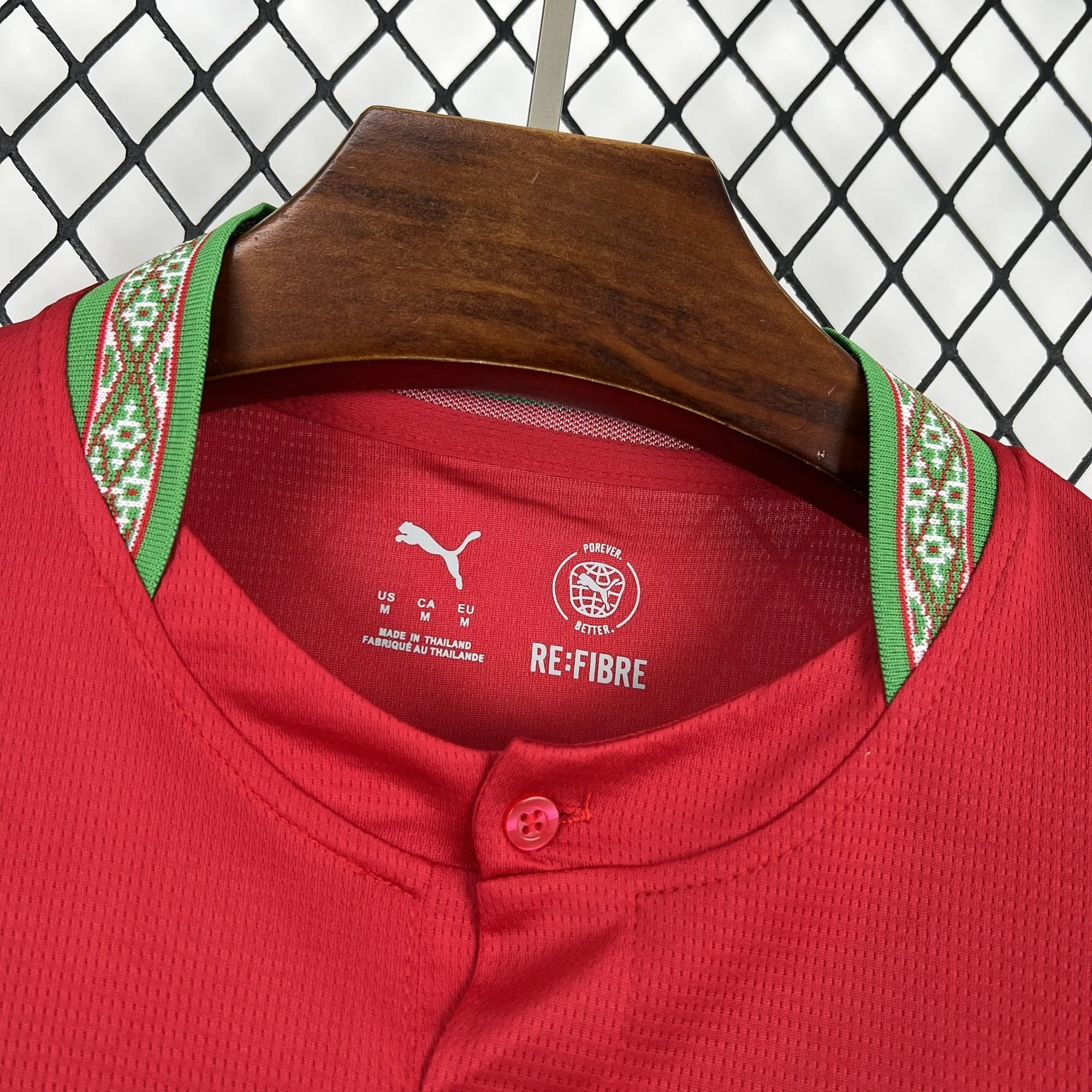 Primer plano del cuello de la camiseta de Marruecos con cierre de un botón, mostrando el diseño interior con la información de talla "M" y la mención a materiales reciclados sobre el tejido rojo.