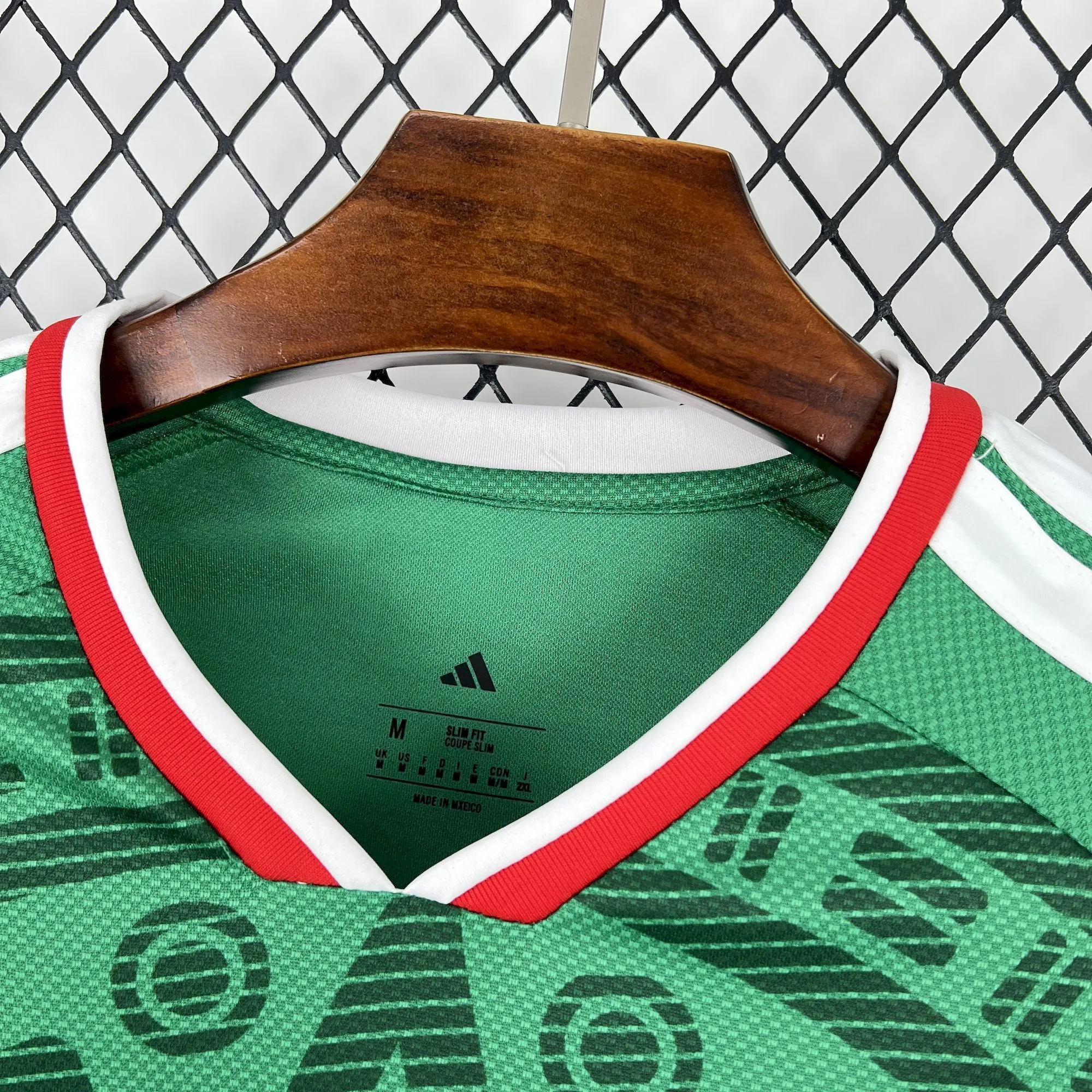 Detalle del interior del cuello en V de la camiseta de México 2026 con ribete rojo y blanco, etiqueta de tallaje M y corte Slim Fit.
