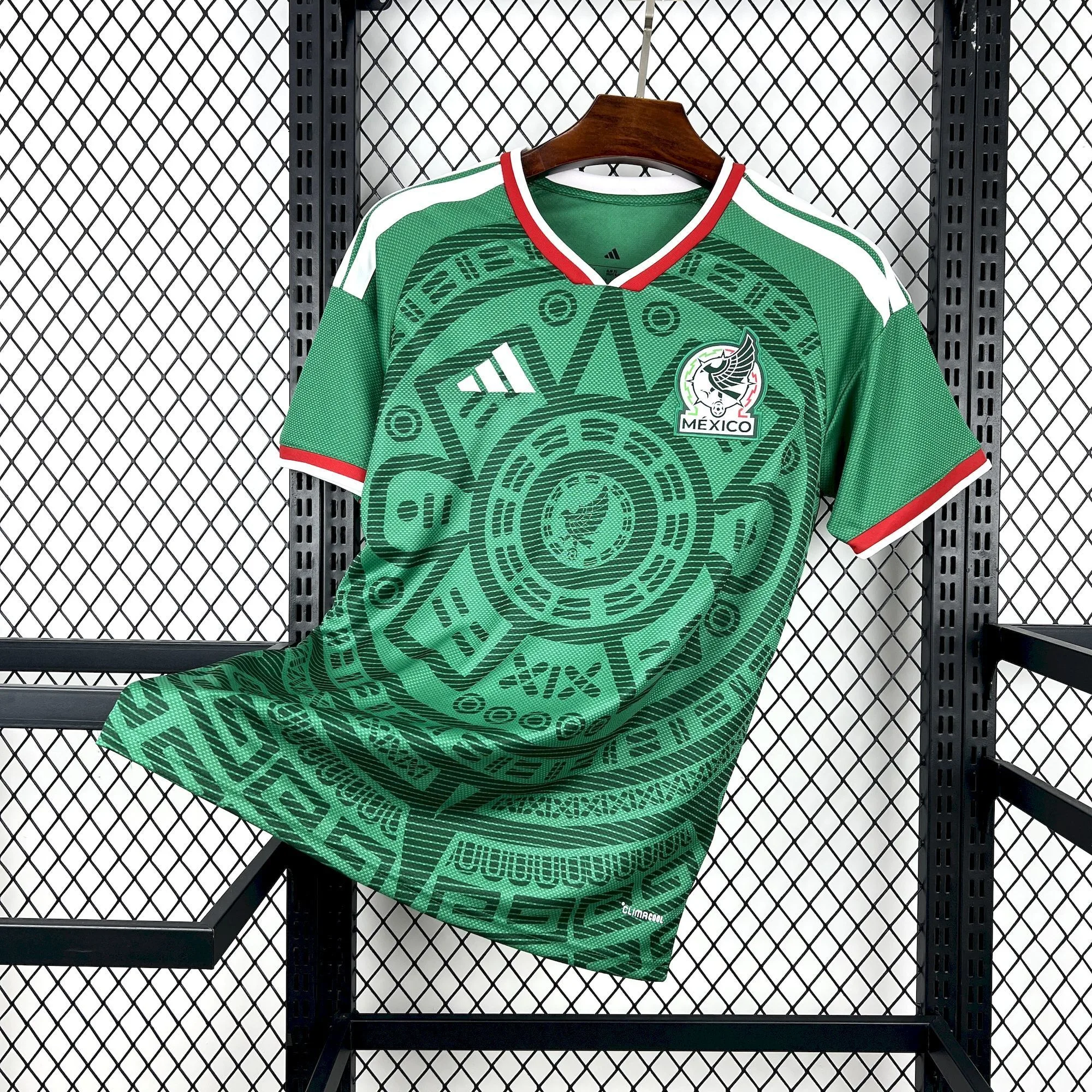 Vista frontal de la camiseta de fútbol de México para el Mundial 2026, verde con un diseño de inspiración azteca en el torso y detalles en rojo y blanco.