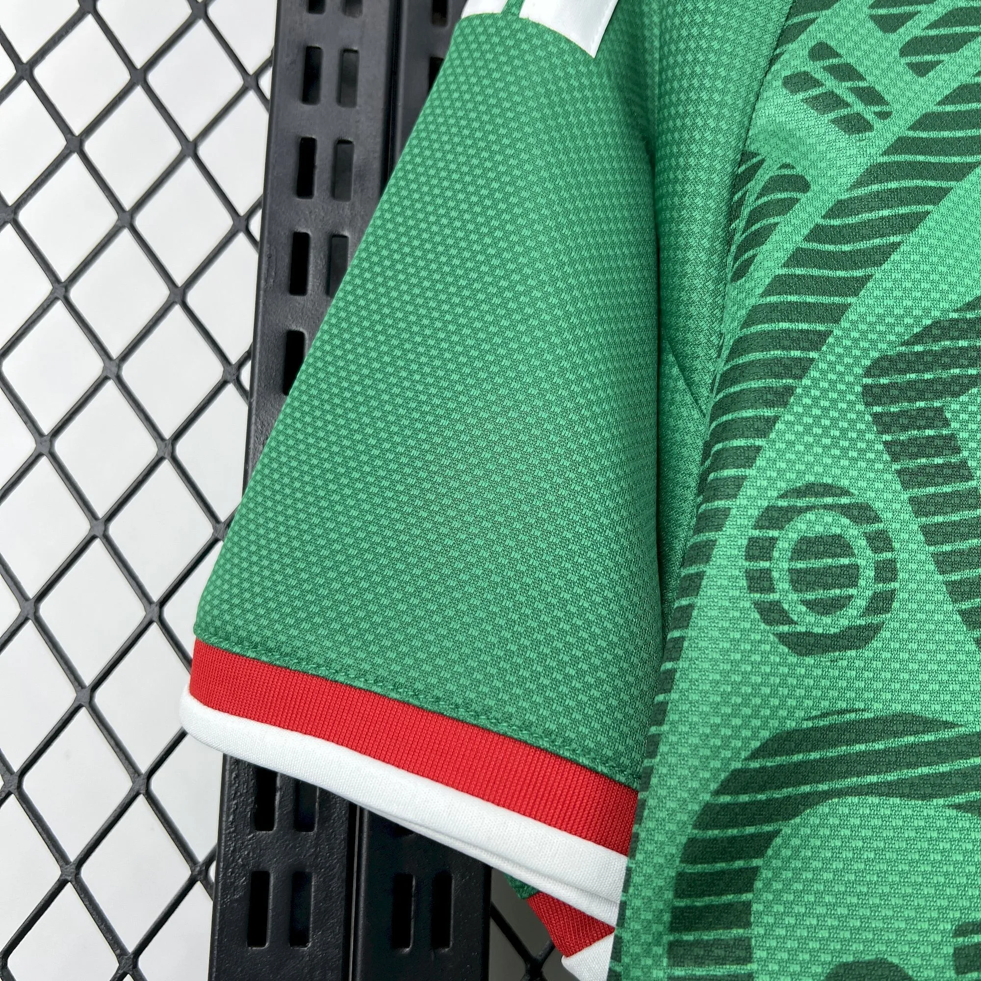 Primer plano del puño de la manga de la camiseta de México para el Mundial 2026, con acabado elástico en rojo y blanco sobre el tejido técnico verde.