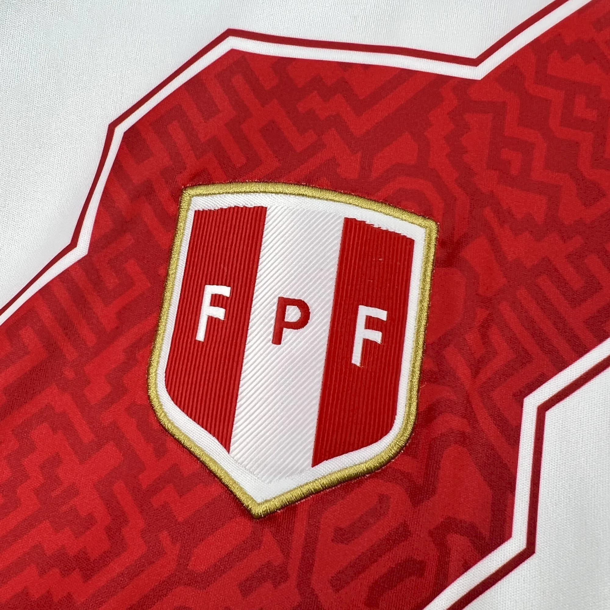 Escudo bordado de la federación de fútbol de Perú sobre el patrón gráfico de la franja roja de la camiseta para el Mundial 2026.