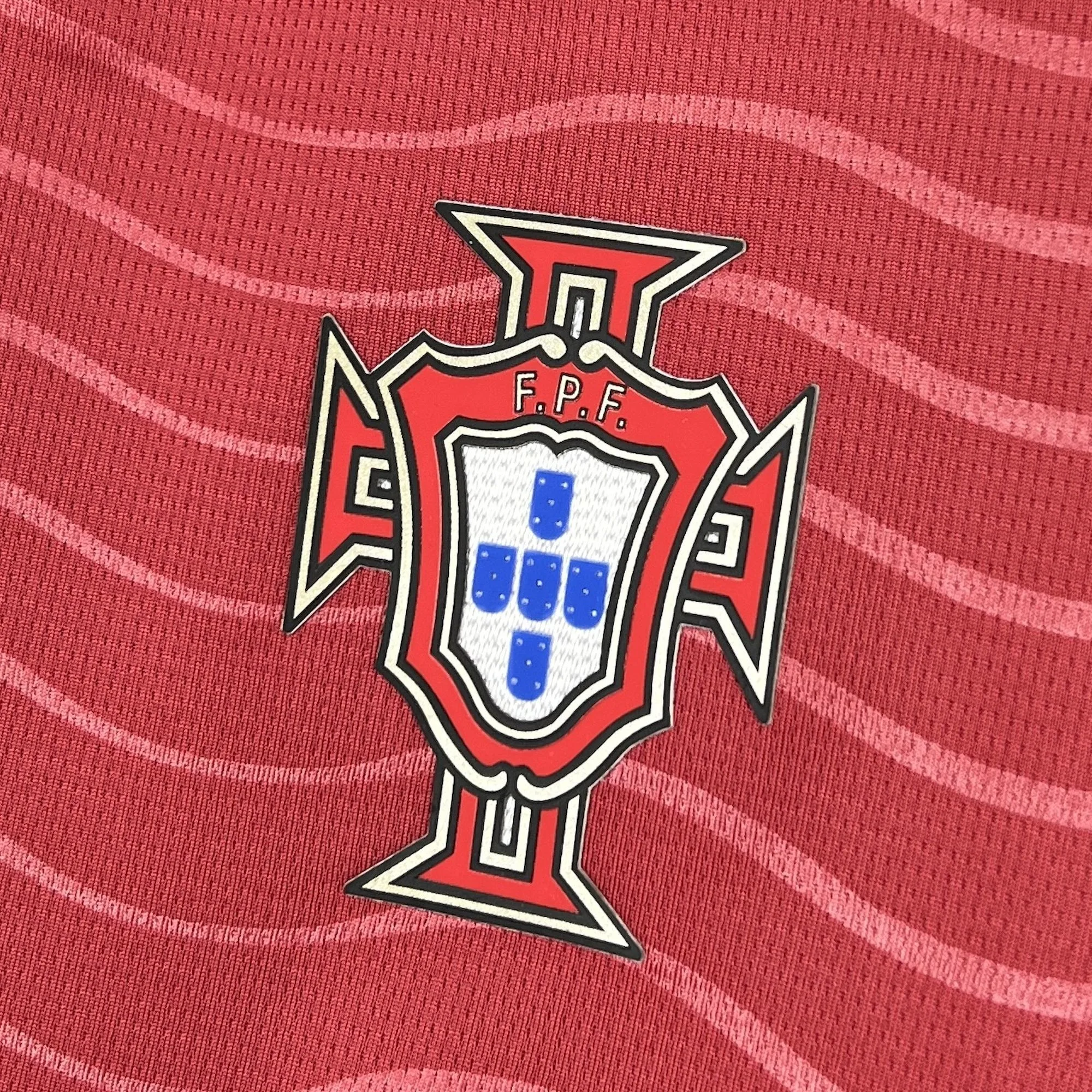 Primer plano del escudo de la Federación Portuguesa de Fútbol (FPF) sobre el diseño de ondas de la camiseta.