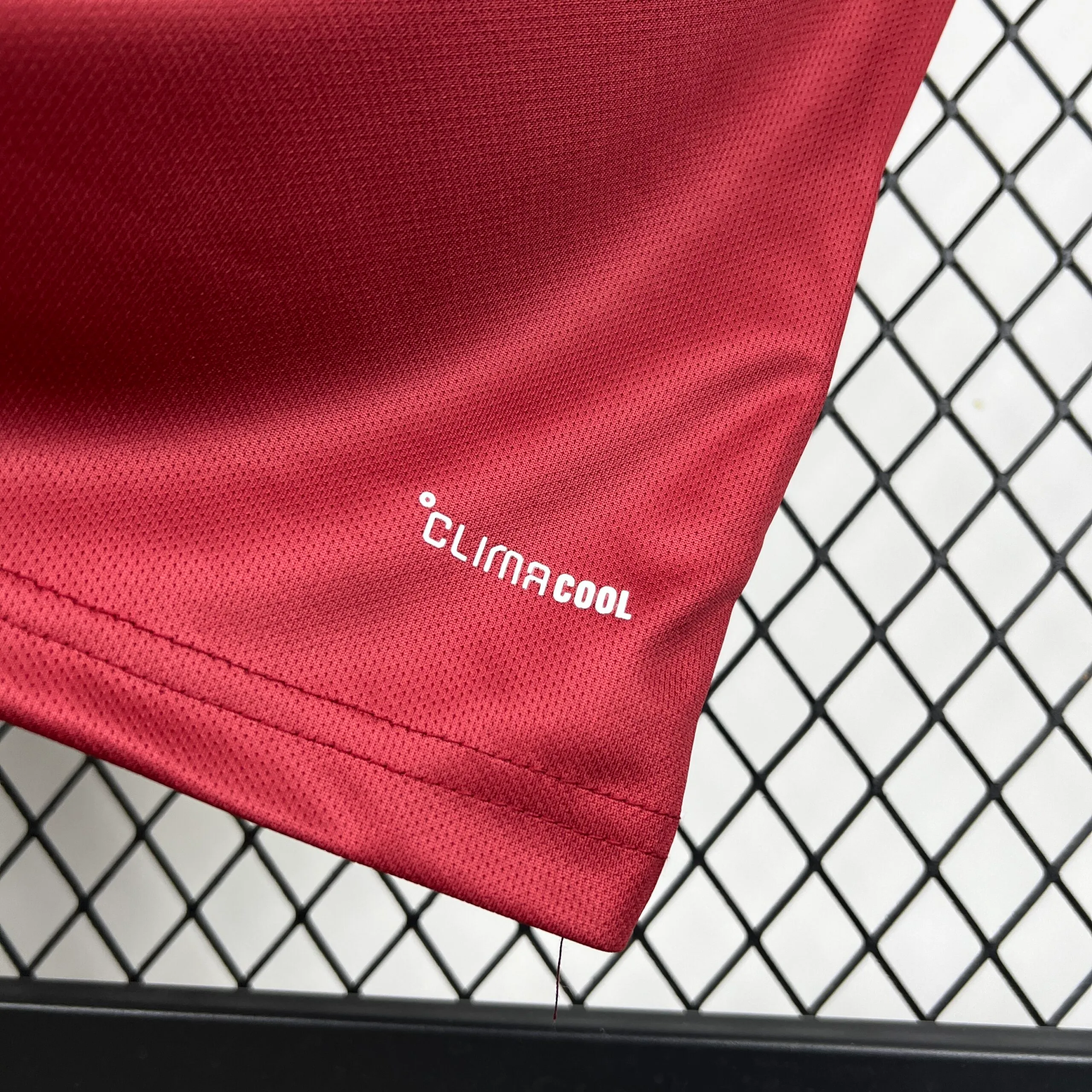 Primer plano de la parte inferior de la camiseta de la selección de Qatar, mostrando el tejido técnico granate y el sello de tecnología "CLIMACOOL" estampado en letras blancas.