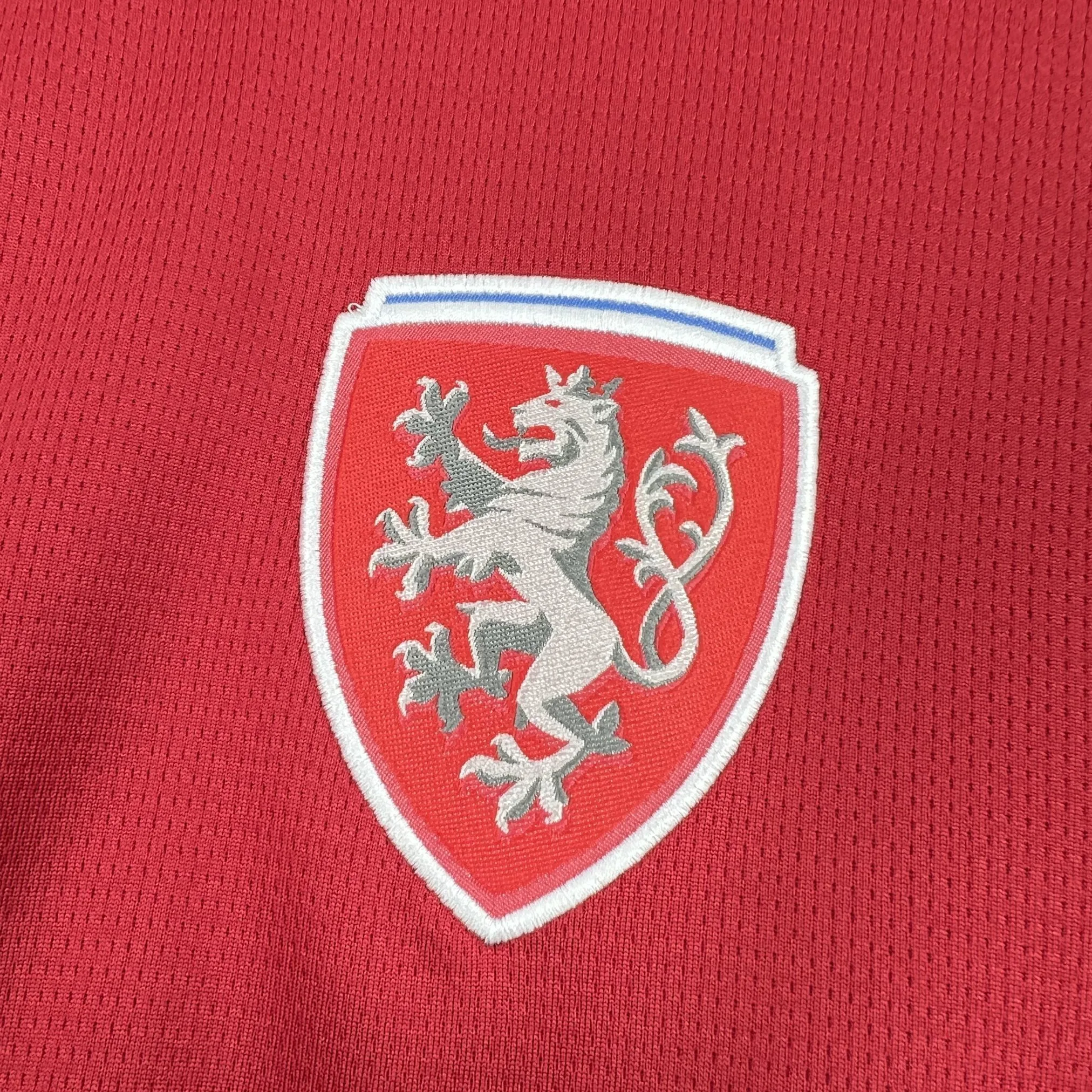 Escudo de la selección nacional de la República Checa bordado en alta definición sobre el tejido técnico rojo para el Mundial 2026.