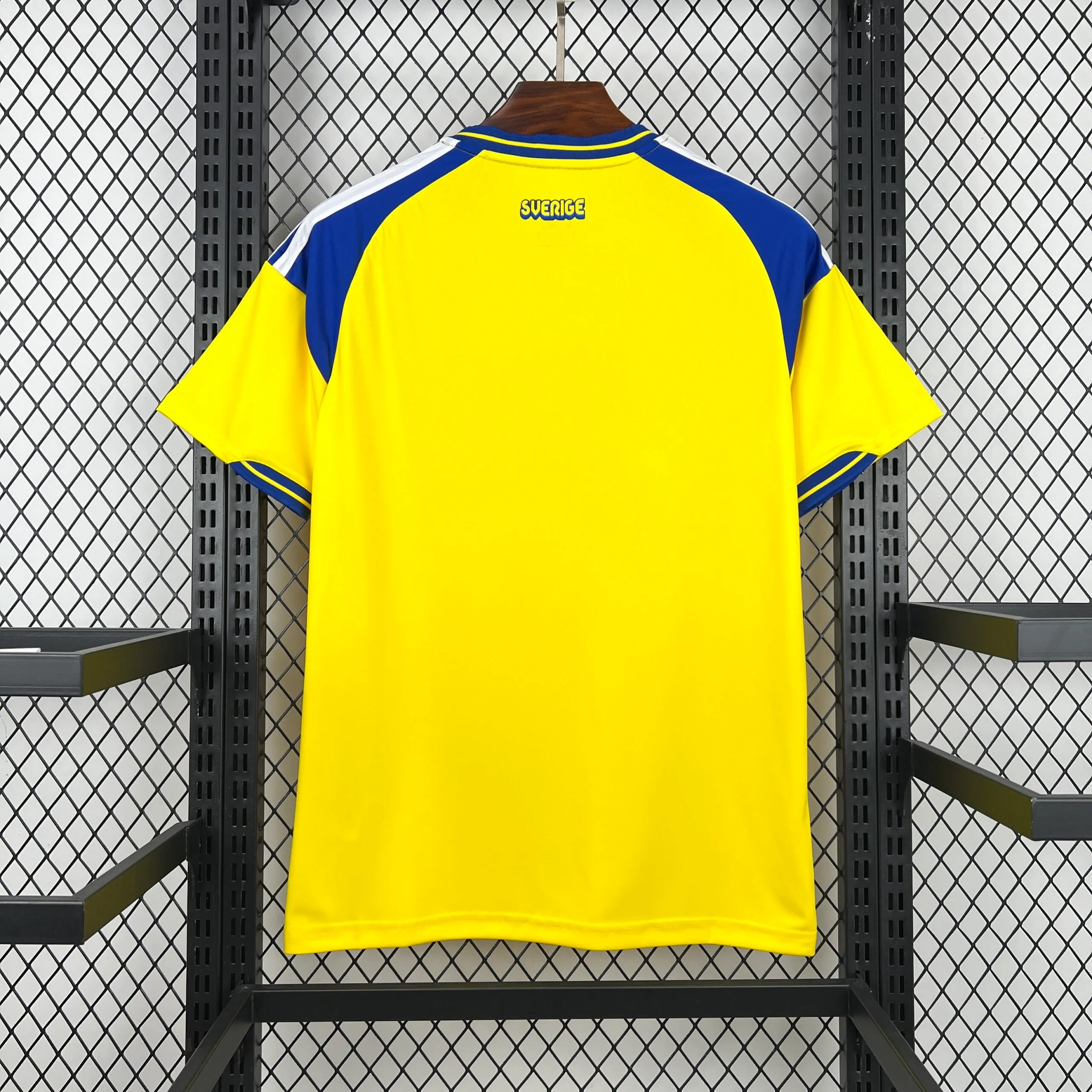 Parte posterior de la camiseta en color amarillo sólido, resaltando los paneles de color azul real en los hombros y la nuca. Justo debajo del cuello, presenta el nombre del país, "SVERIGE", estampado en letras azules con borde amarillo.