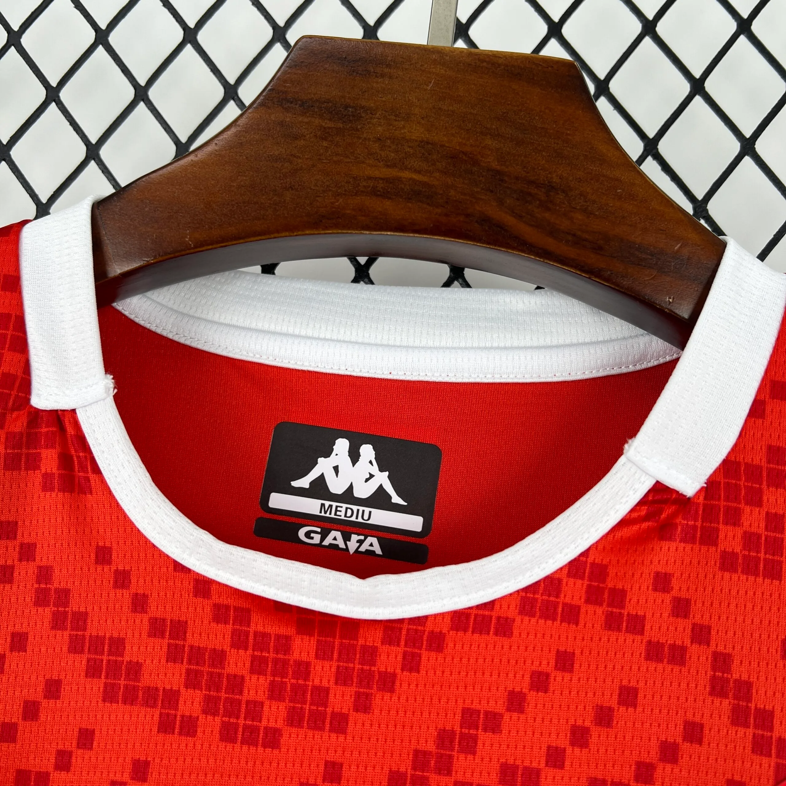 Primer plano del cuello redondo blanco de la camiseta de la selección de Túnez, mostrando la etiqueta interna estampada con el logotipo de la marca, la talla "MEDIUM" y la línea de diseño.