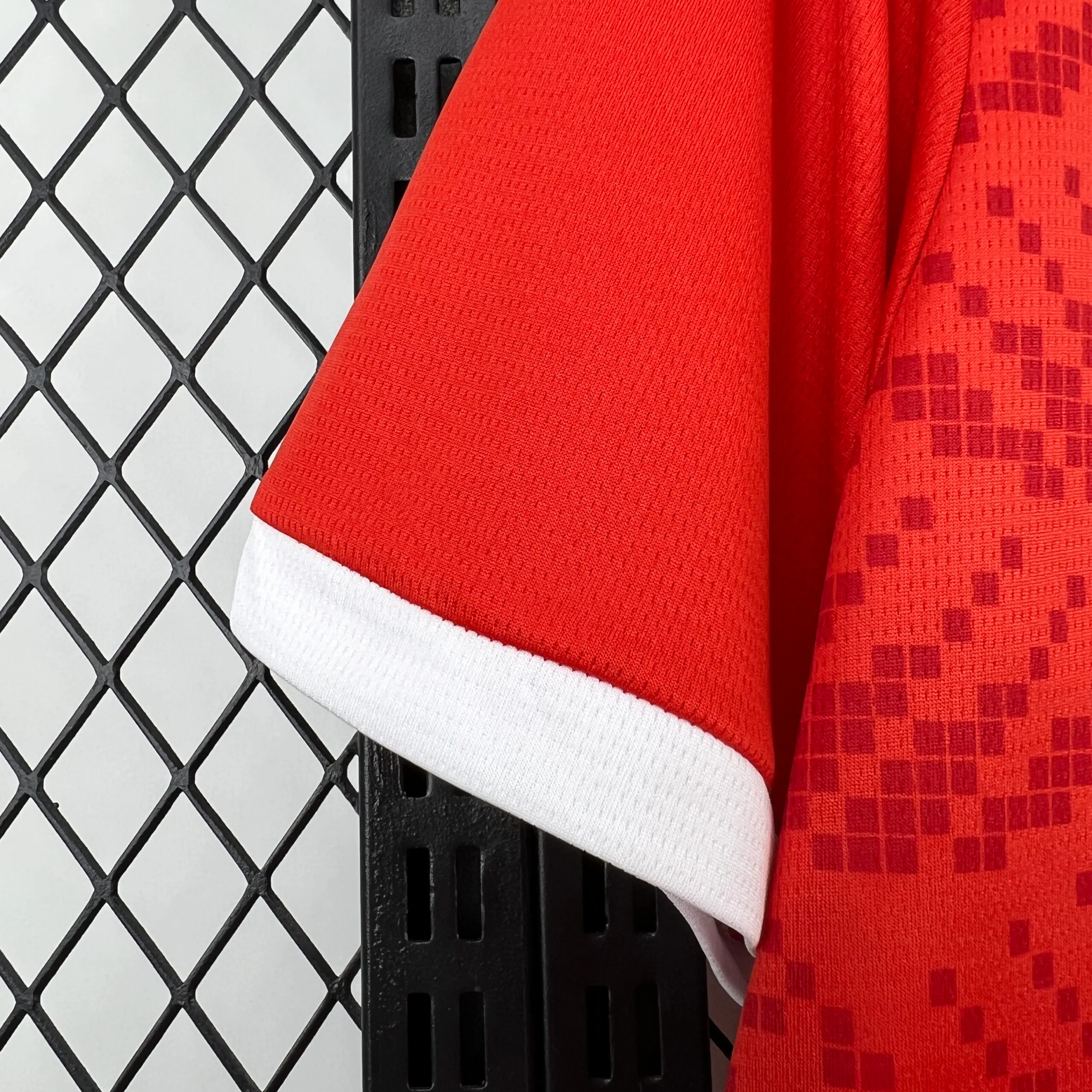 Primer plano de la manga corta de la camiseta de la selección de Túnez, mostrando el tejido técnico en color rojo y el remate del puño en una banda ancha de color blanco.