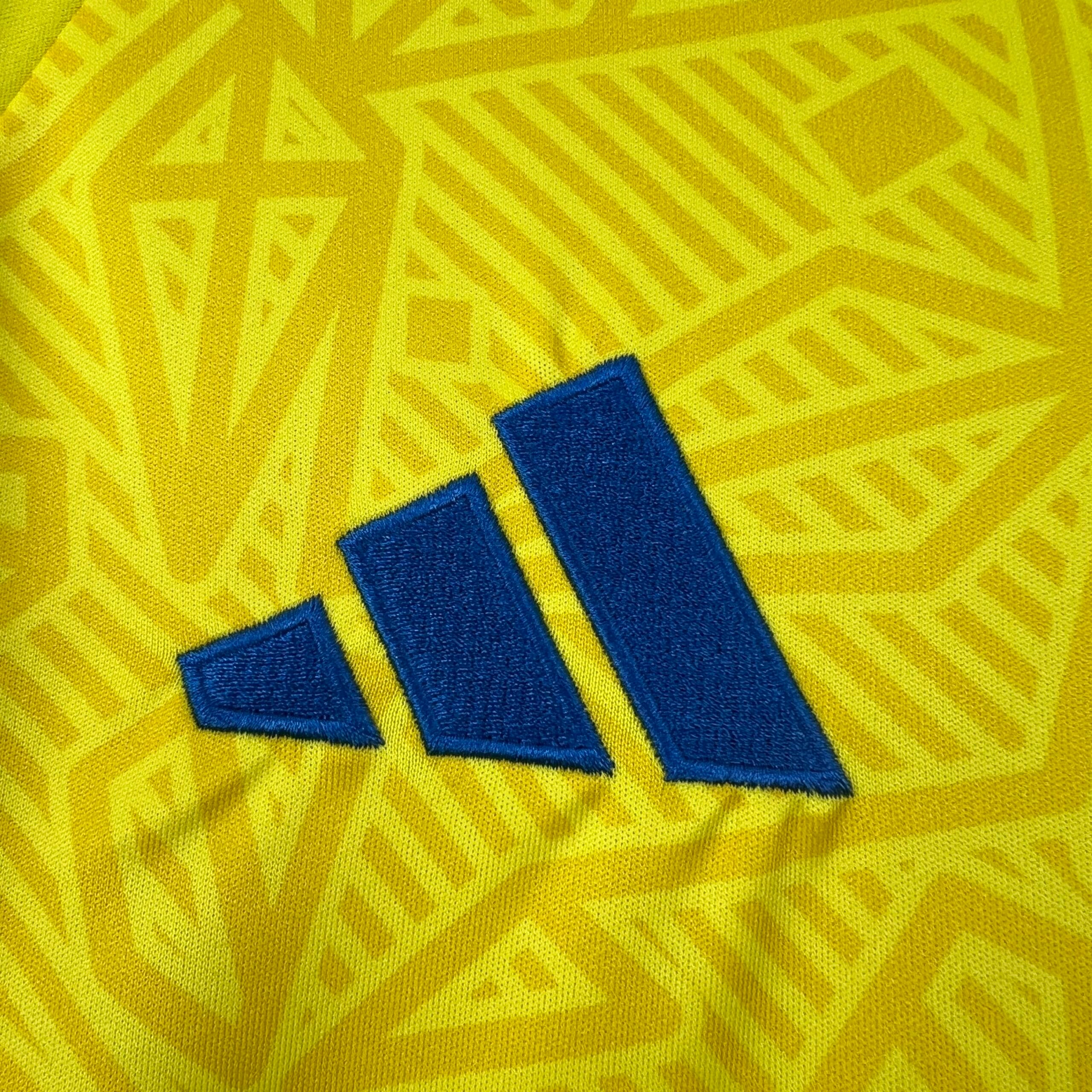 Detalle de elemento decorativo bordado en color azul sobre el patrón geométrico de la camiseta.