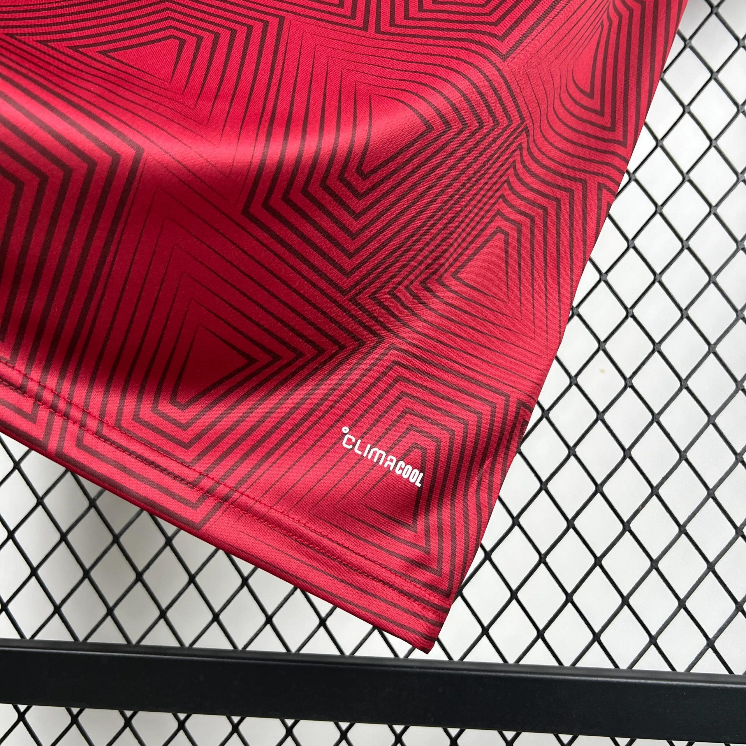 Primer plano de la parte inferior de la camiseta de la selección de Venezuela, mostrando la continuidad del patrón de cuadros concéntricos en color vino tinto y el sello de tecnología "CLIMACOOL" estampado en letras blancas cerca del borde.