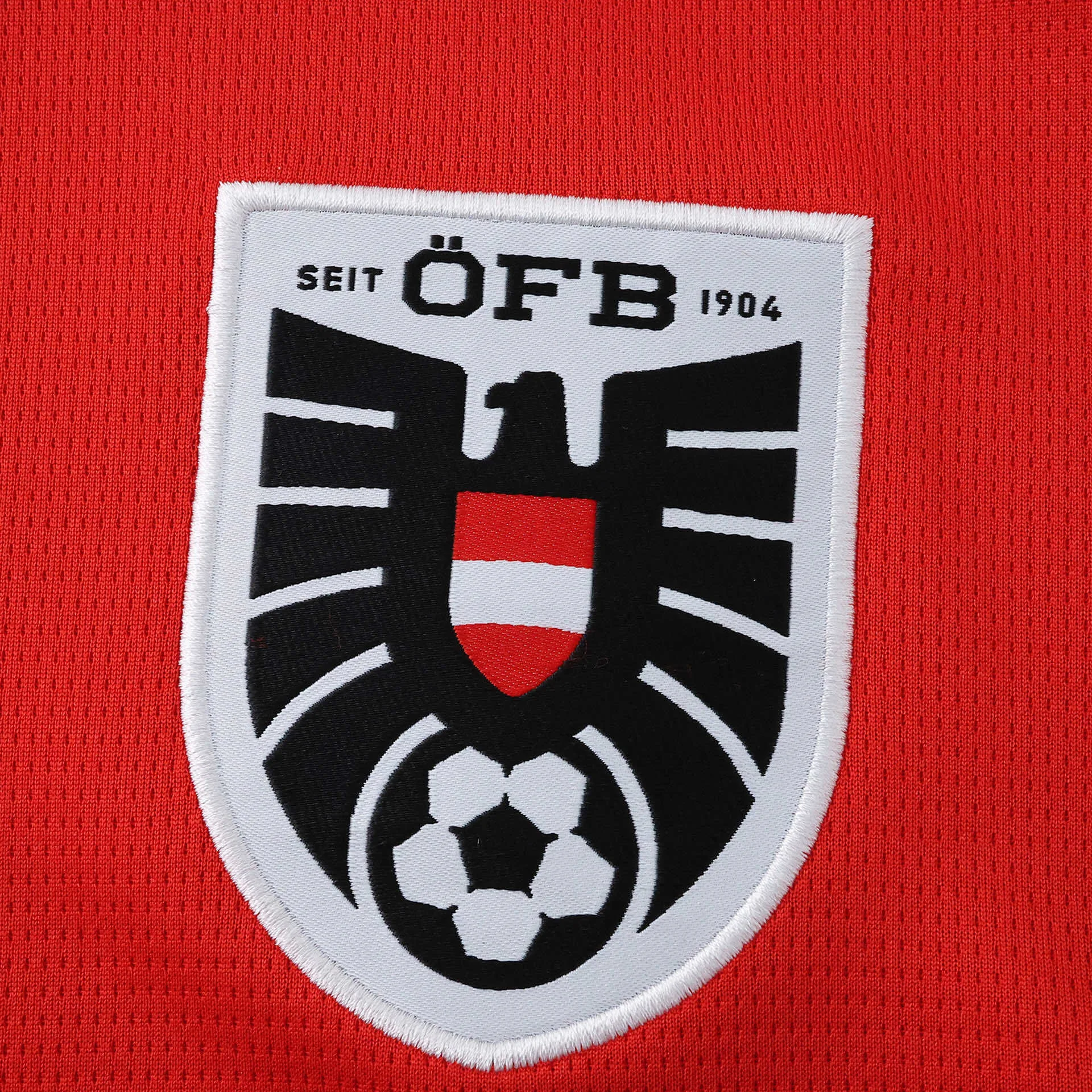 Primer plano del escudo de la federación austriaca (ÖFB) con el águila negra sobre fondo rojo y blanco.