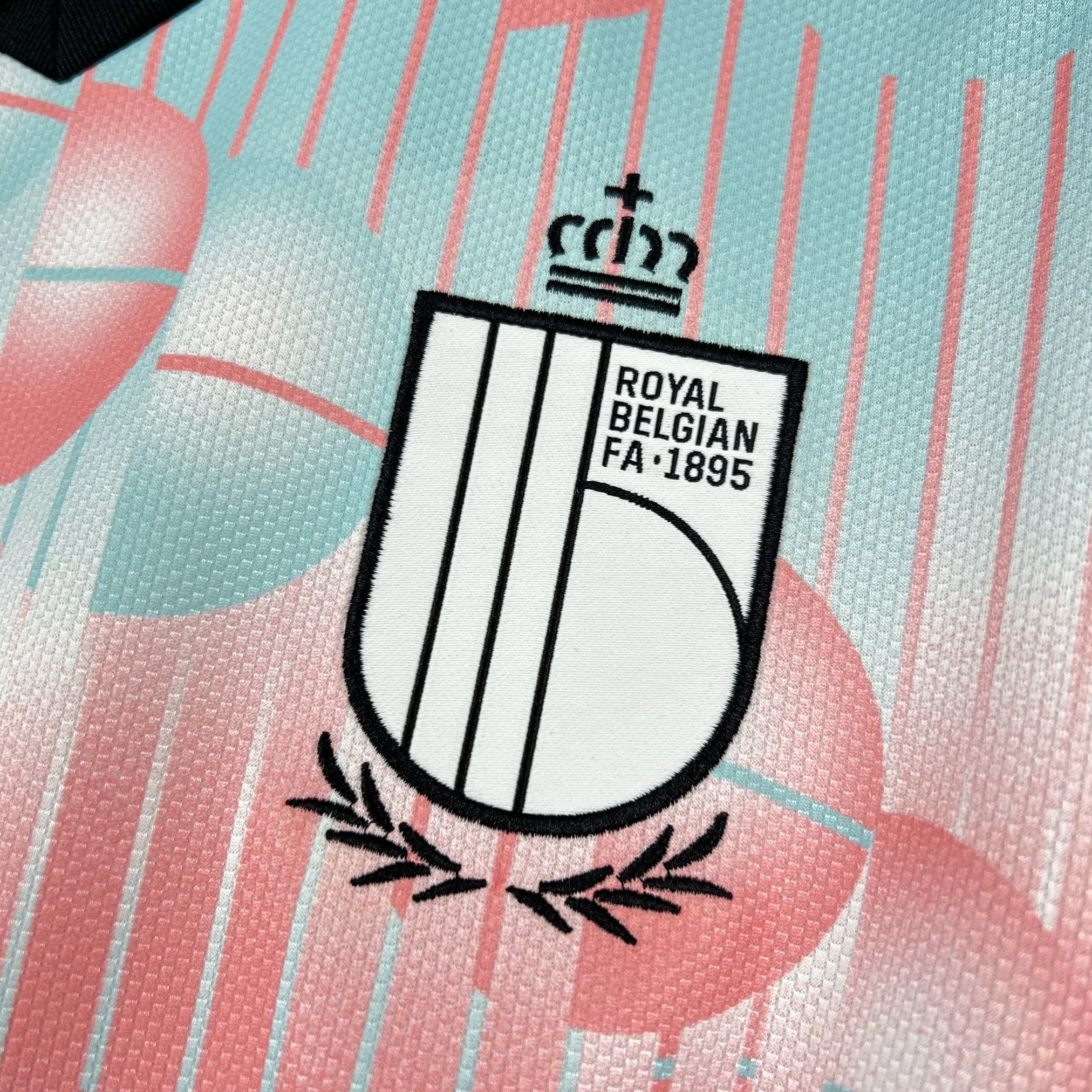 Primer plano del escudo de la Real Federación Belga de Fútbol bordado en dorado sobre el fondo azul celeste.
