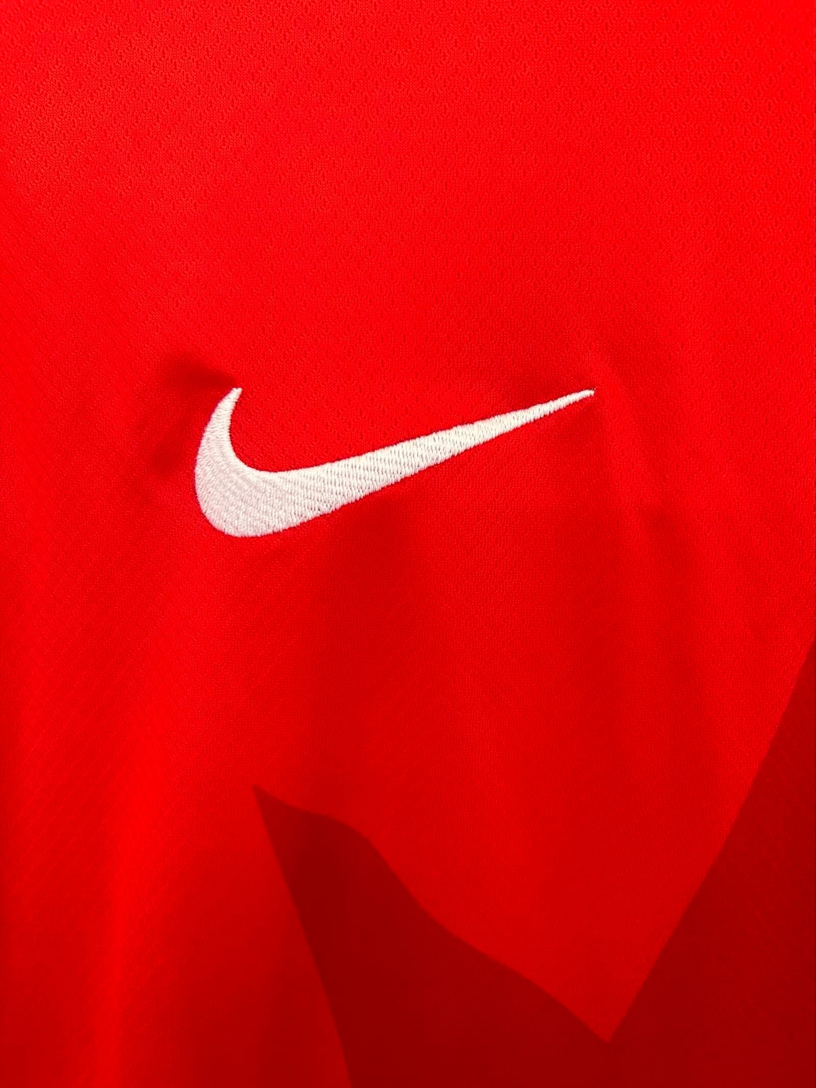 Detalle de logotipo decorativo bordado en color blanco sobre el tejido técnico rojo de la camiseta canadiense.