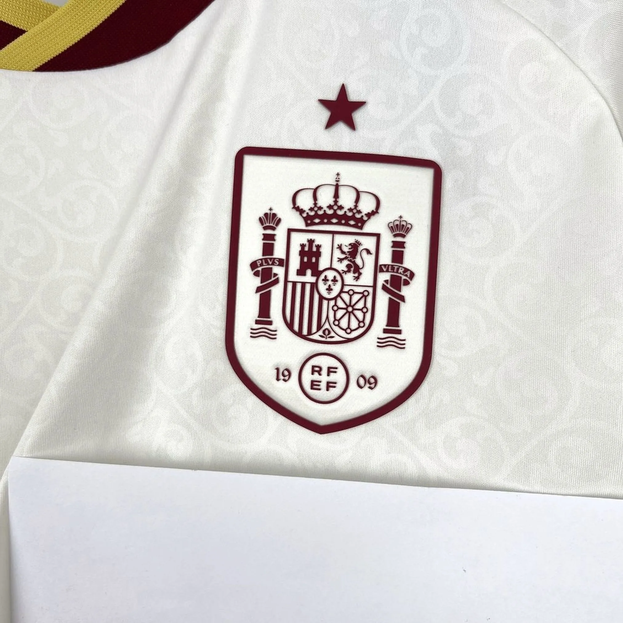 Primer plano del escudo de la selección española de fútbol bordado en amarillo sobre fondo azul marino.