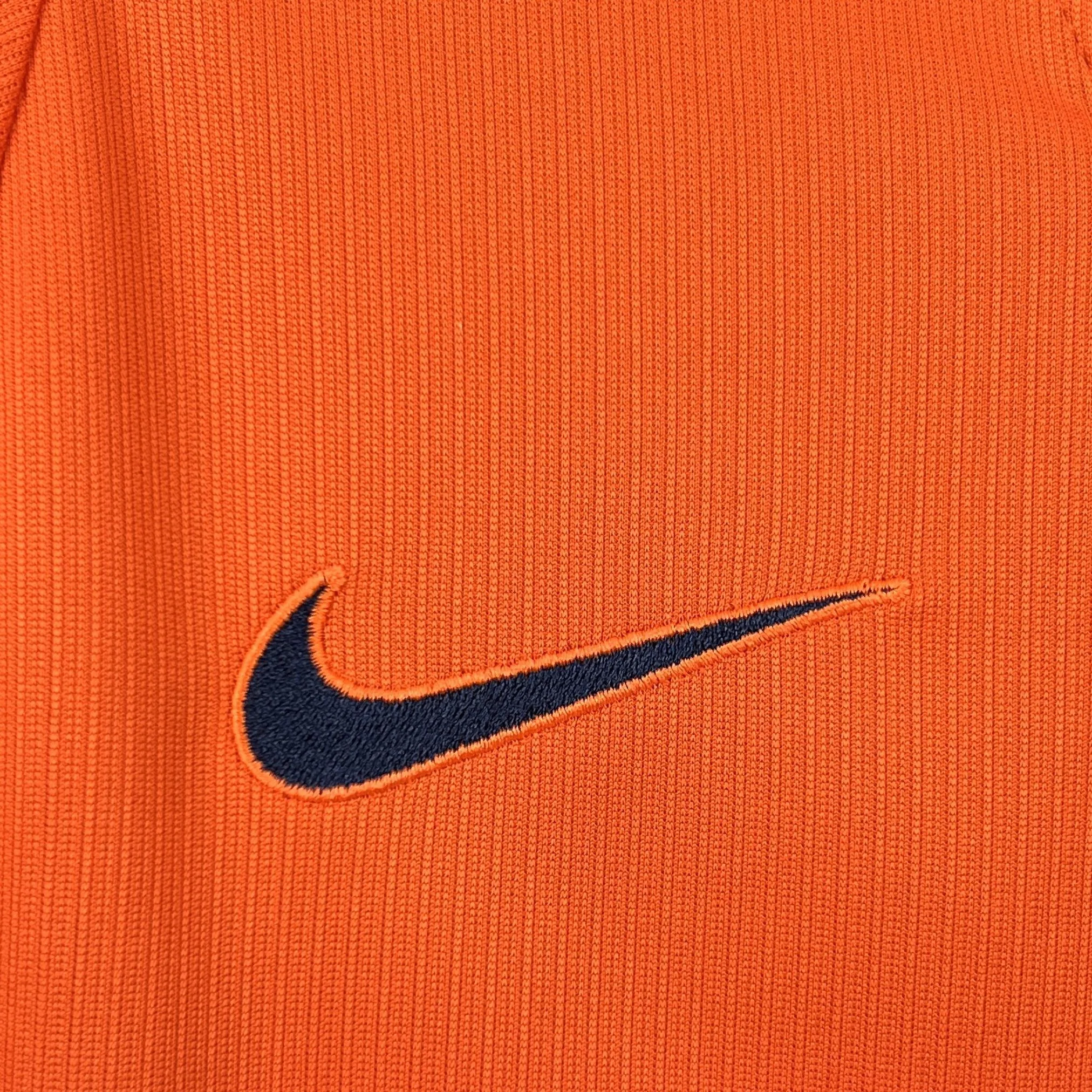 Detalle de elemento decorativo bordado en color negro sobre el pecho de la camiseta naranja.