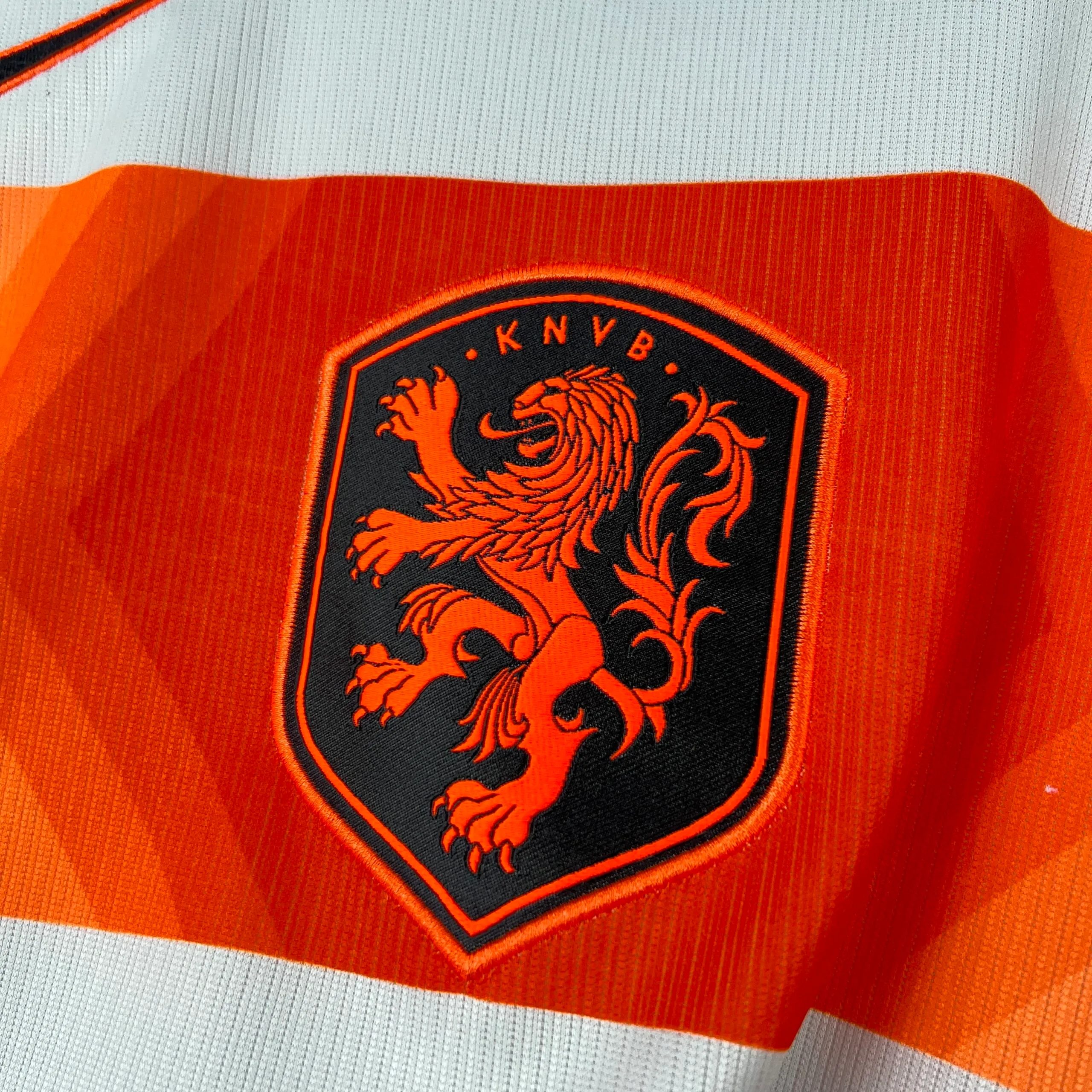 Primer plano del escudo del león de la KNVB bordado en naranja sobre el tejido azul de la equipación.