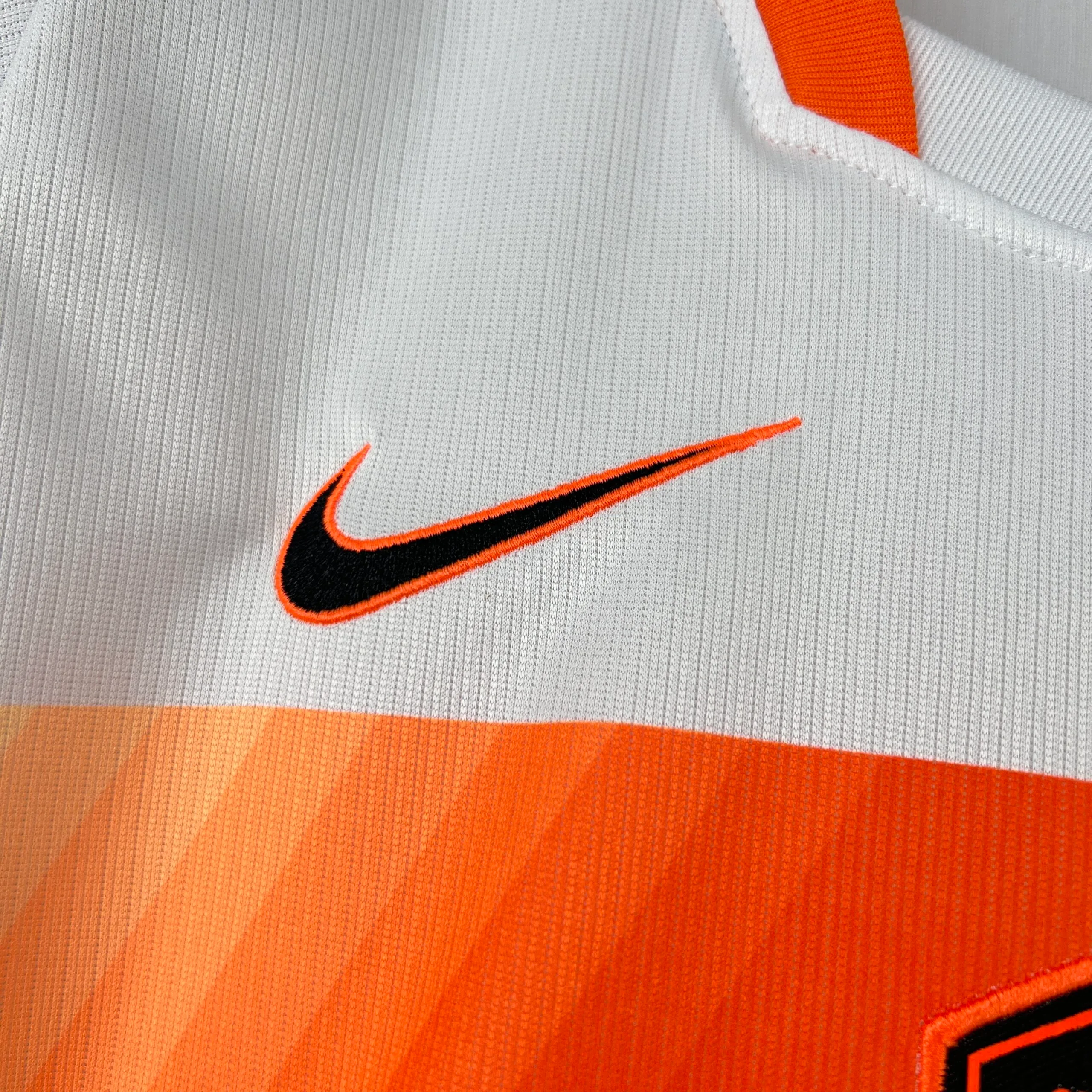 Detalle de elemento decorativo bordado en color naranja sobre el fondo azul de la camiseta nacional.