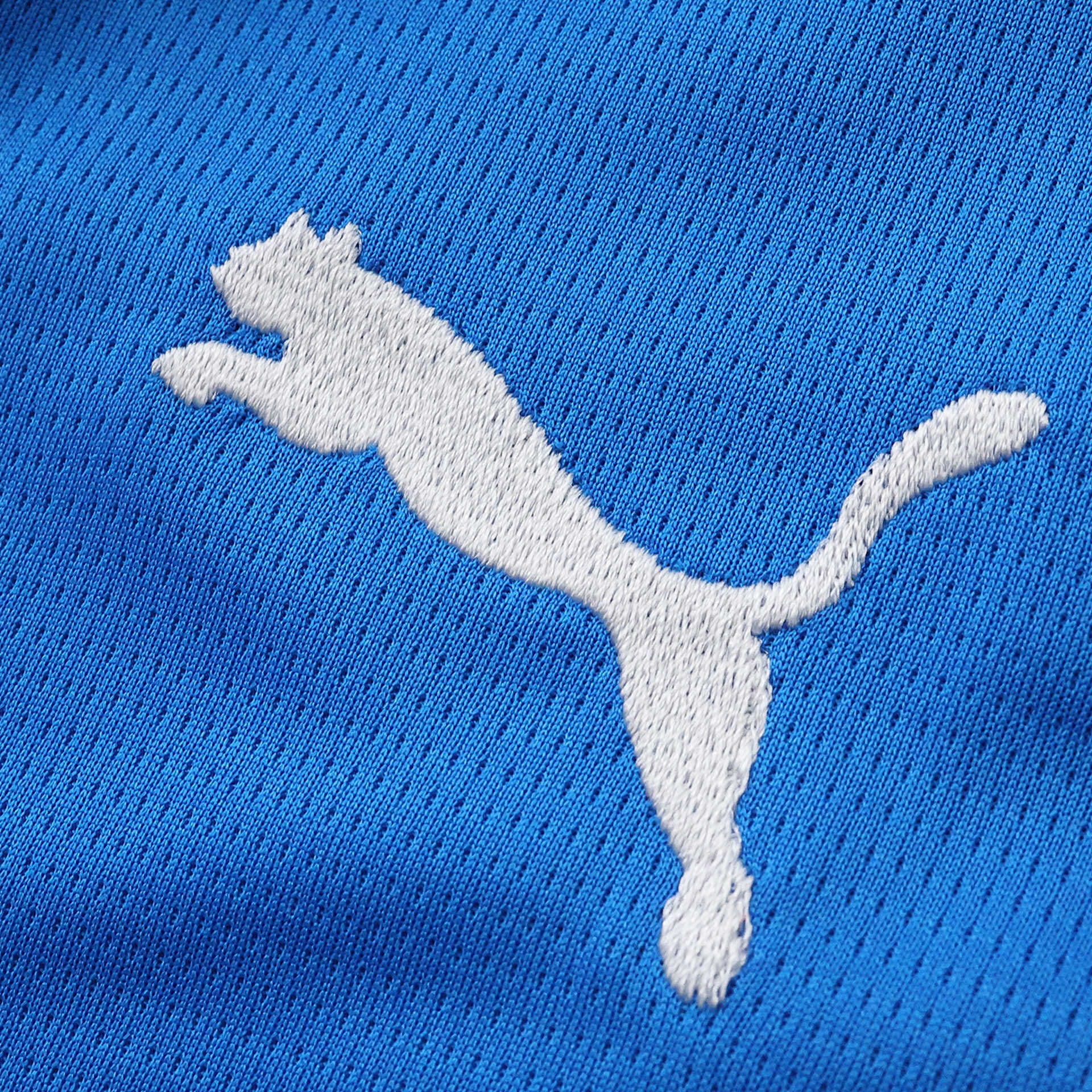 Detalle de logotipo decorativo blanco bordado sobre el tejido calado de la prenda.