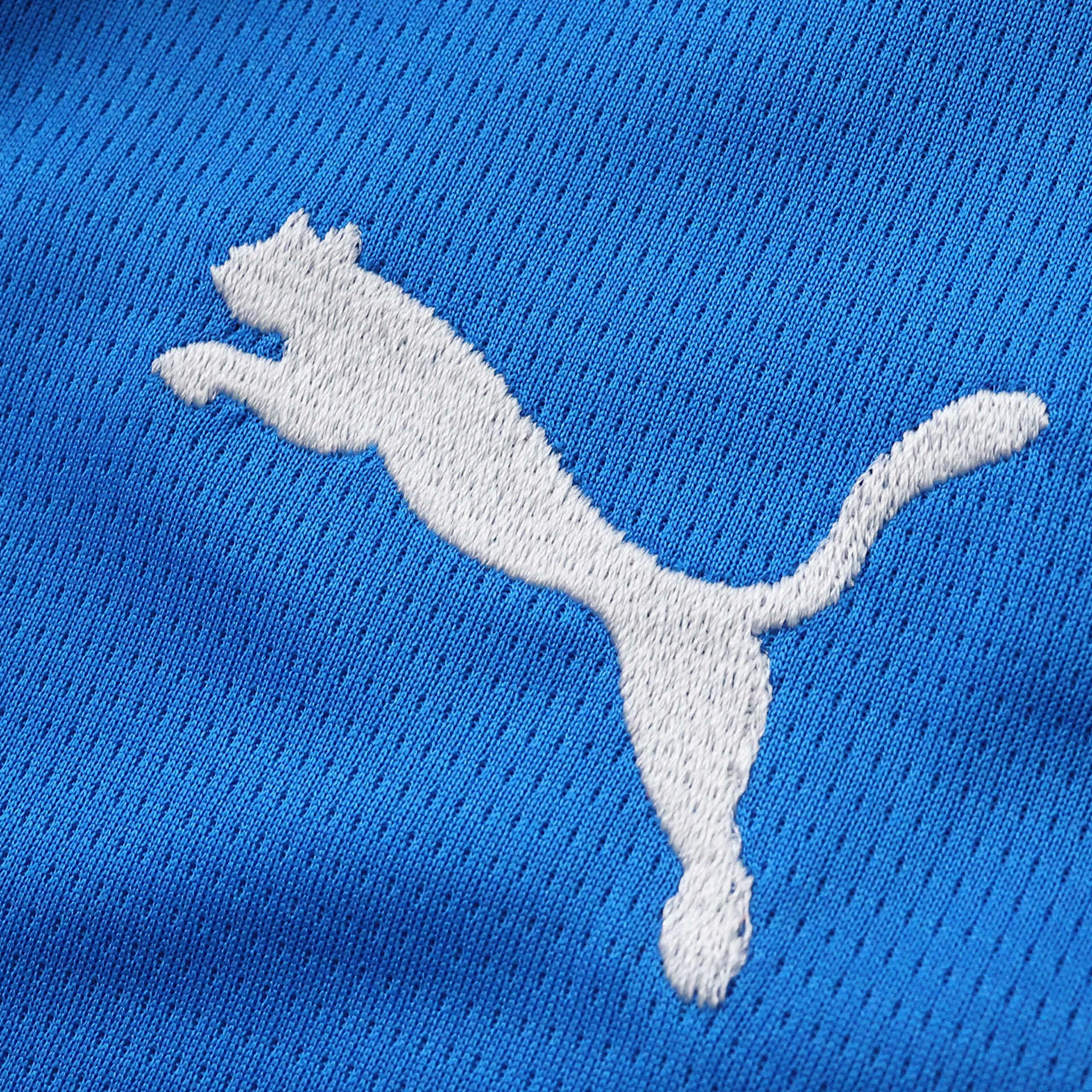 Detalle de logotipo decorativo blanco bordado sobre el tejido calado de la prenda.